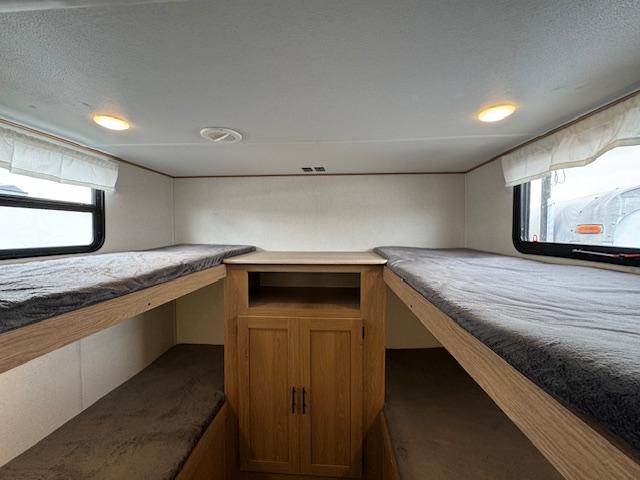 RV rental's cozy bunk room: two sets of bunk beds with grey linens, and a central wooden cabinet.. Prime Time Avenger 2023