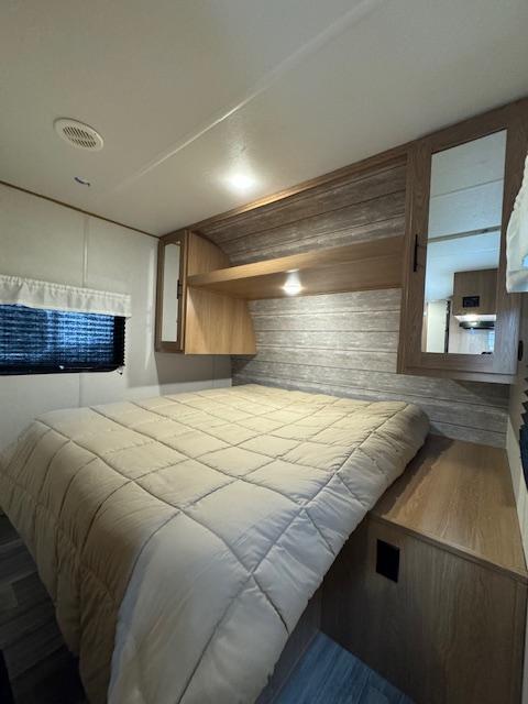 Cozy RV rental bedroom featuring a large bed with a beige comforter, wood-paneled walls, and built-in storage.. Prime Time Avenger 2023