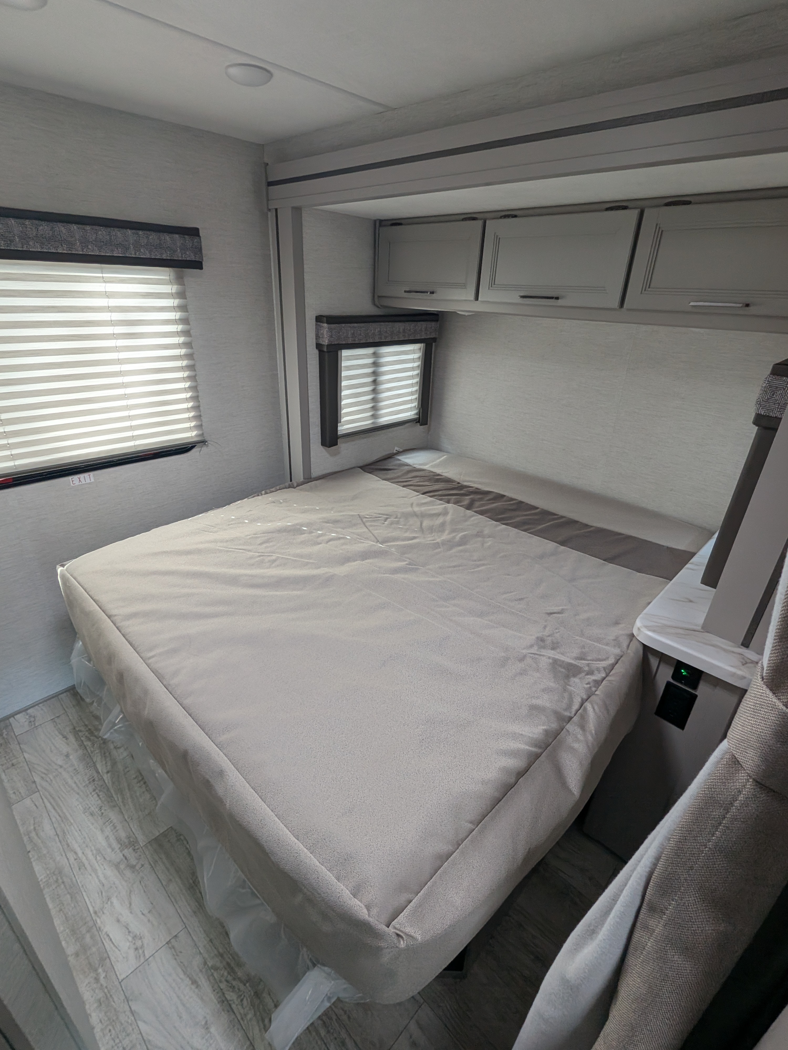 RV rental bedroom interior: a light gray bed, overhead cabinets, and windows with blinds create a modern, clean space.. Thor Motor Coach Chateau 2025