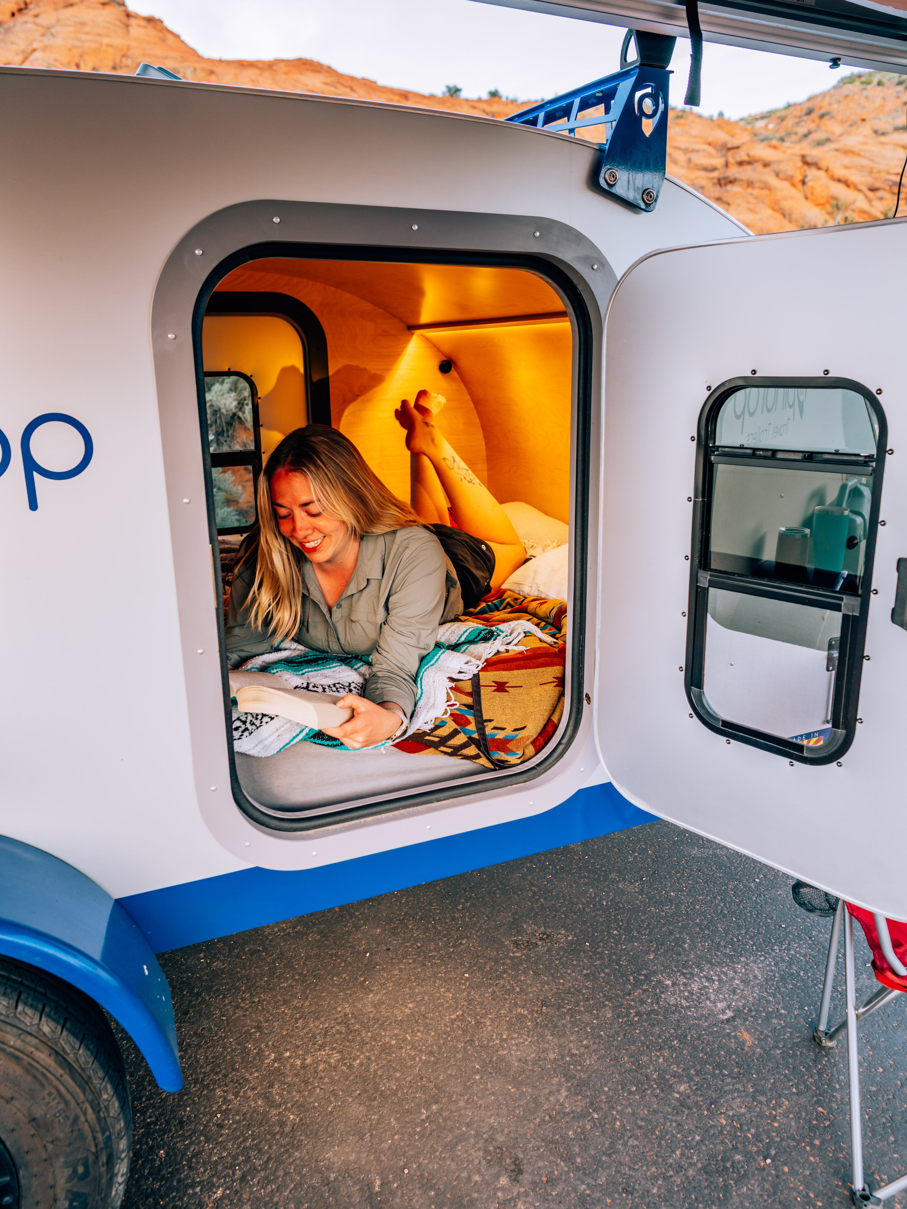 Woman reads in a cozy GoLoop RV rental. Experience comfort in a compact travel trailer, perfect for your next adventure.. Pindrop Travel Trailer Fina Roma 2022