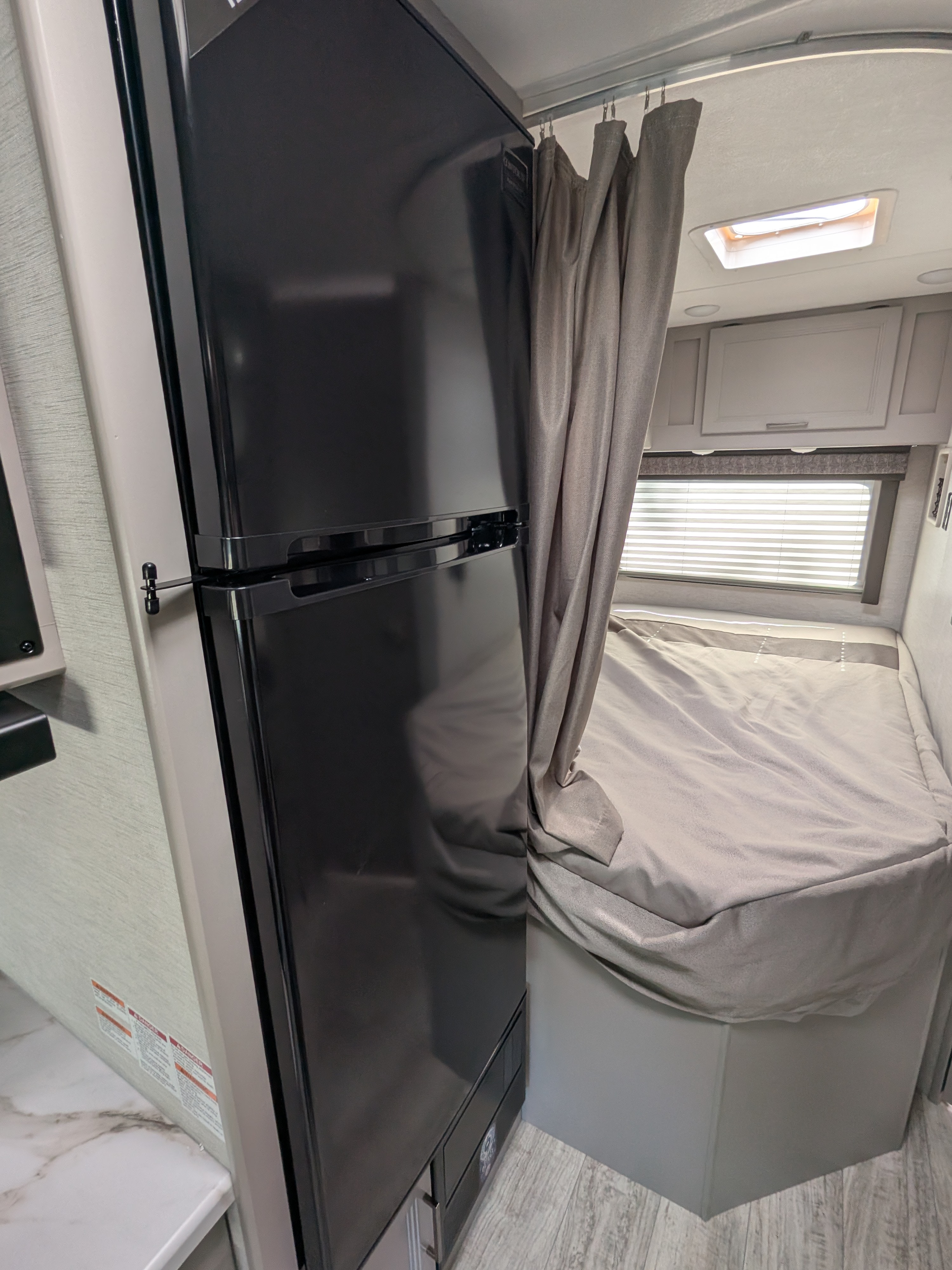This RV rental offers a compact kitchen area with a black refrigerator, adjacent to a curtained sleeping space with a bed.. Thor Motor Coach Chateau 2025
