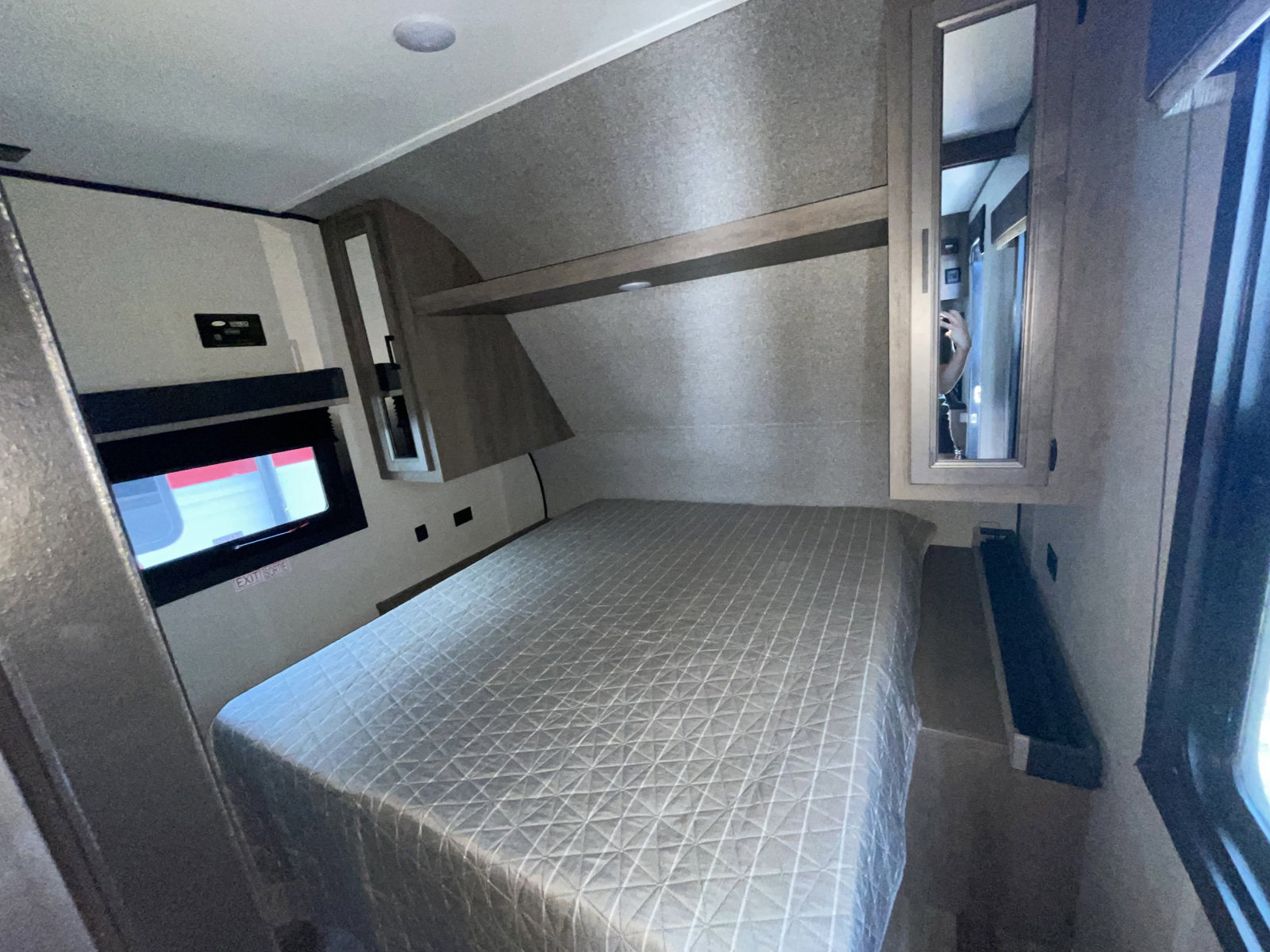 Modern bedroom in an RV rental, featuring a comfy bed with quilted cover, window, and mirrored cabinet. Ideal for travel.. Highland Ridge RV Open Range 2022