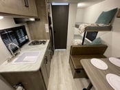 RV rental interior shows a compact kitchen with sink and stovetop, a dinette, and bunk beds, perfect for family travel.. Keystone Springdale 2024