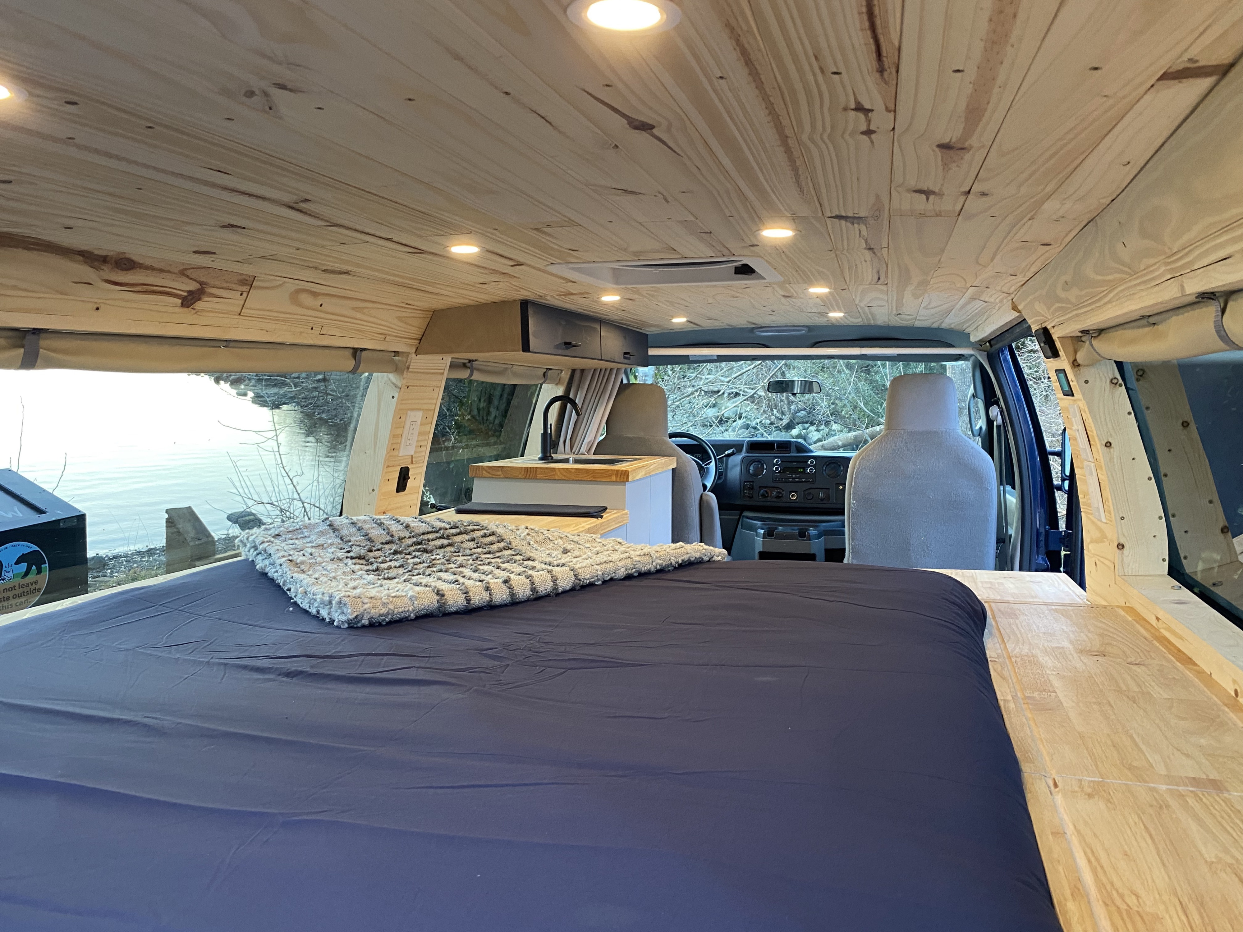 Cozy RV rental interior: custom wood ceiling, comfy bed, sink, and scenic views. Perfect for van life adventures.. Ford Econoline Club Wagon 2010