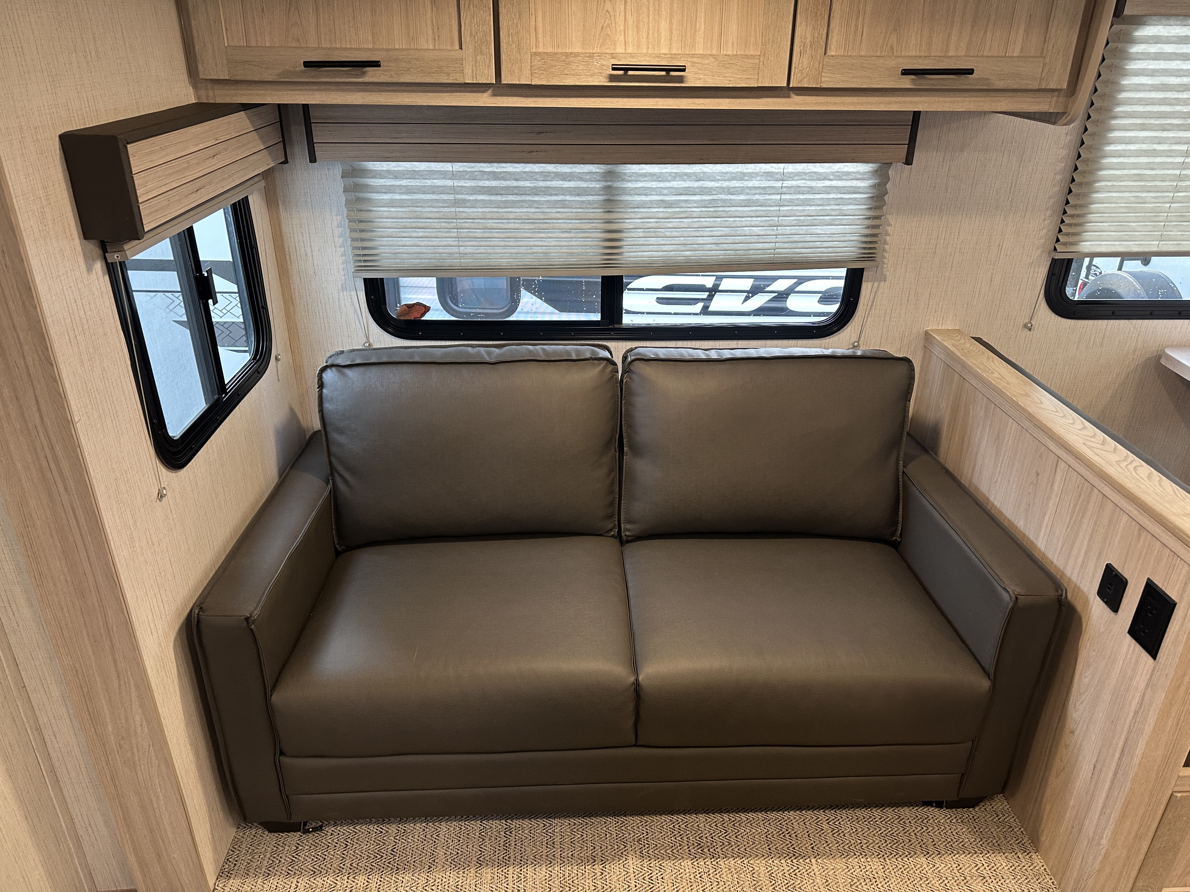 Cozy RV rental interior featuring a gray sofa, light wood cabinets, and windows with blinds, ideal for travel.. Cruiser RV Shadow Cruiser 2022