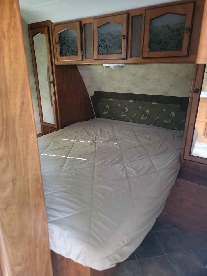 Experience comfort in this RV rental bedroom with a neatly made bed, wood cabinetry, and a mirrored closet.. Keystone RV Passport Ultra Lite 2012