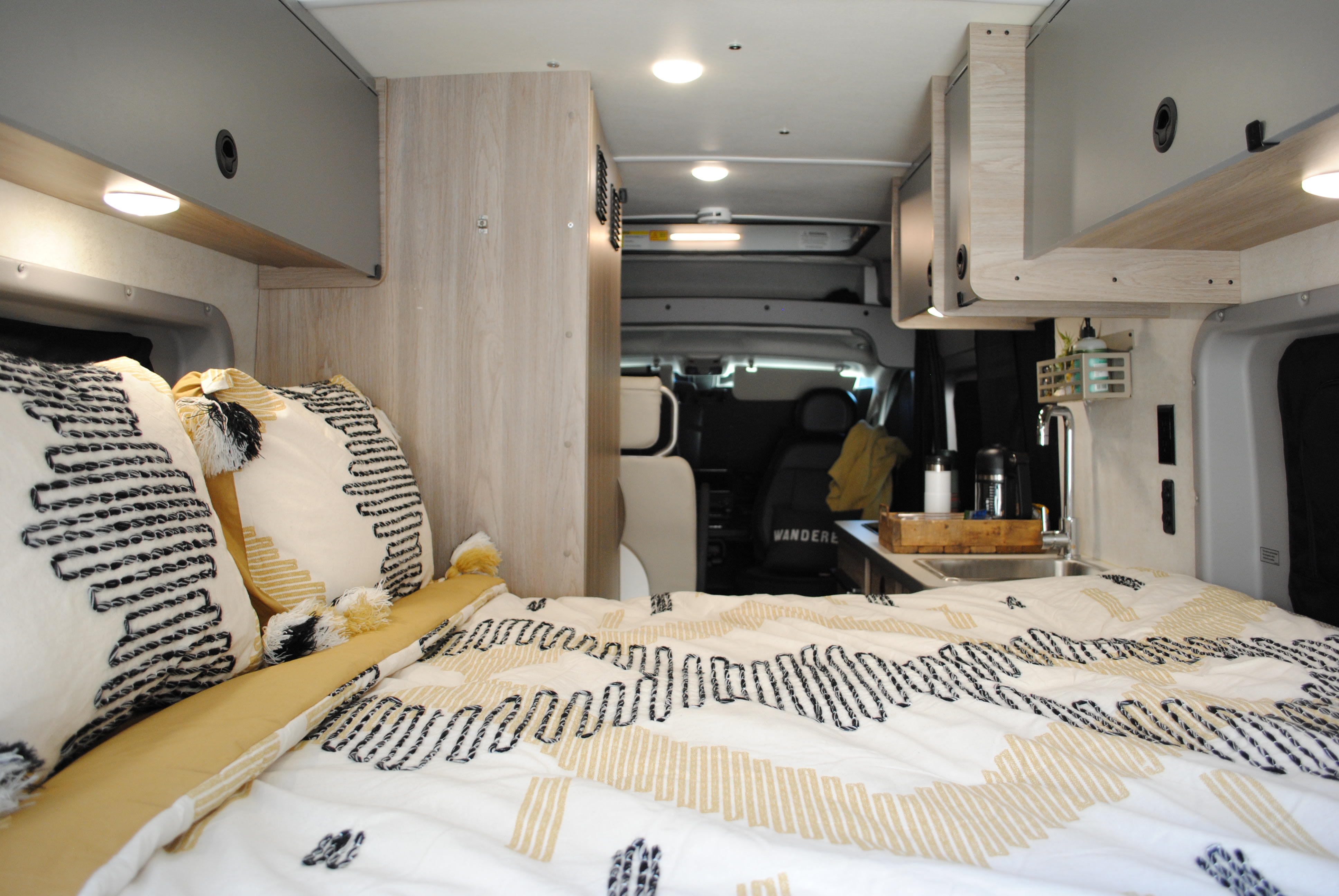 This inviting RV rental interior features a cozy bed with stylish bedding, overhead storage, and a compact kitchen area.. Winnebago Solis 2023