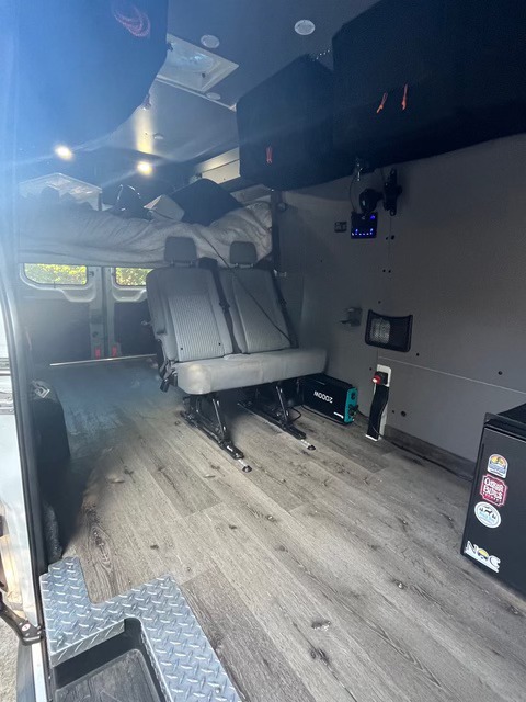 RV rental camper van interior: elevated bed, track seating, wood-look floor, and mobile power for versatile travel.. Ford F350 2015