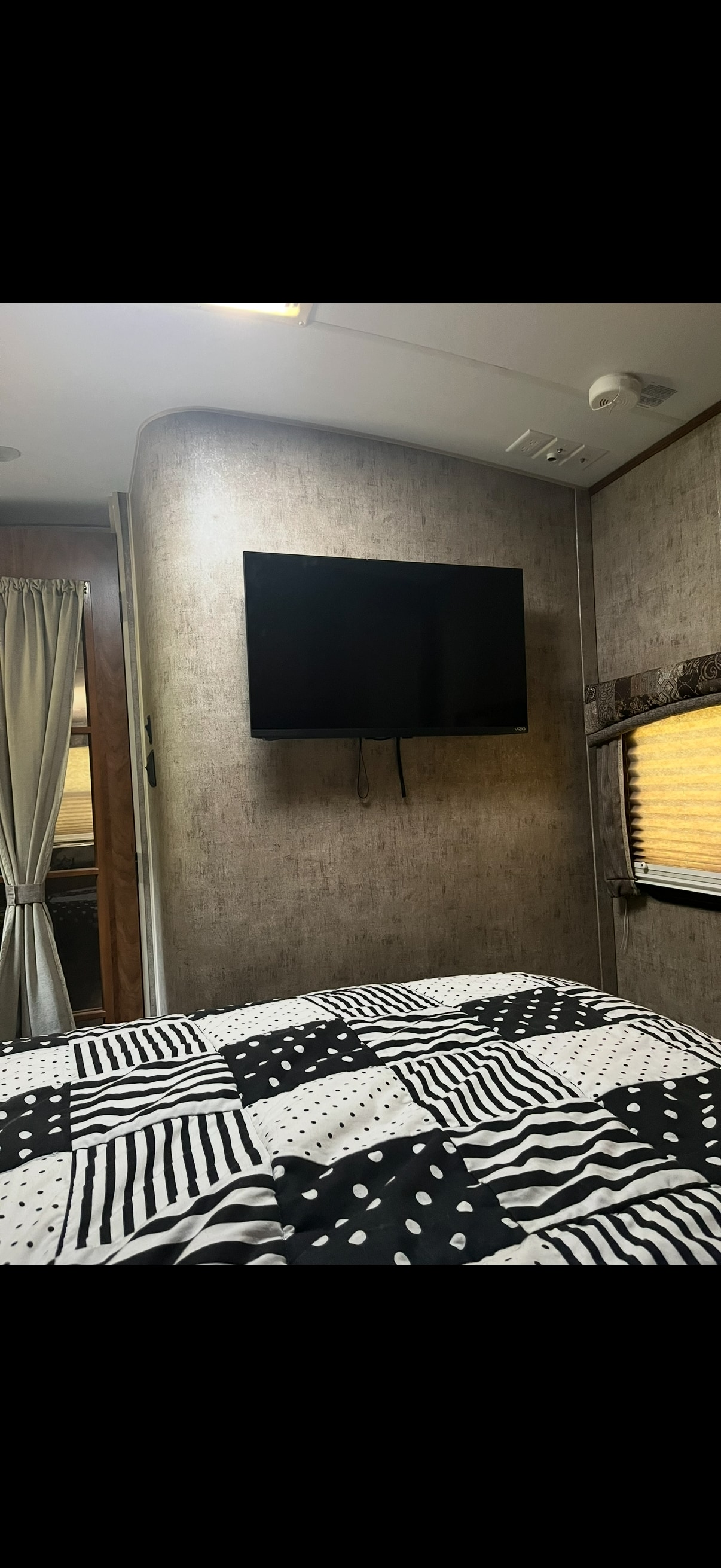 Cozy RV rental bedroom features a patterned bed, mounted TV, and window blinds, perfect for travel.. Outdoors RV Wind River 250rdsw 2014