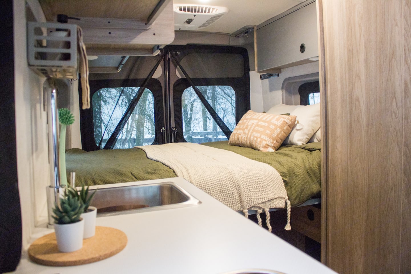 This RV rental interior offers a cozy bed, compact kitchen, and views of snowy trees for your trip.. Winnebago Solis 2023