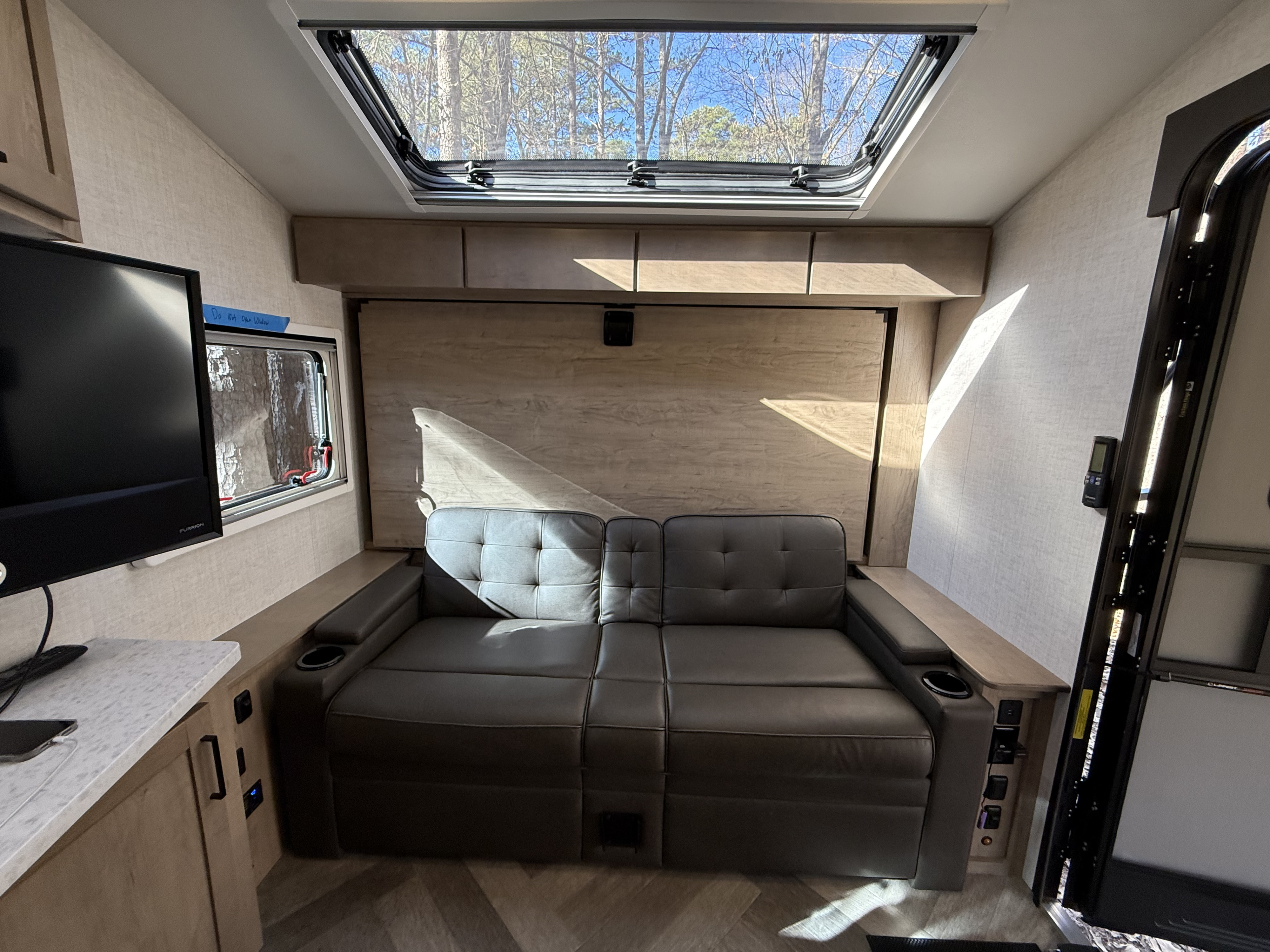 Cozy RV rental interior, showing a sofa, TV, and large skylight with views of trees. A comfortable living space.. Ember Overland 2023