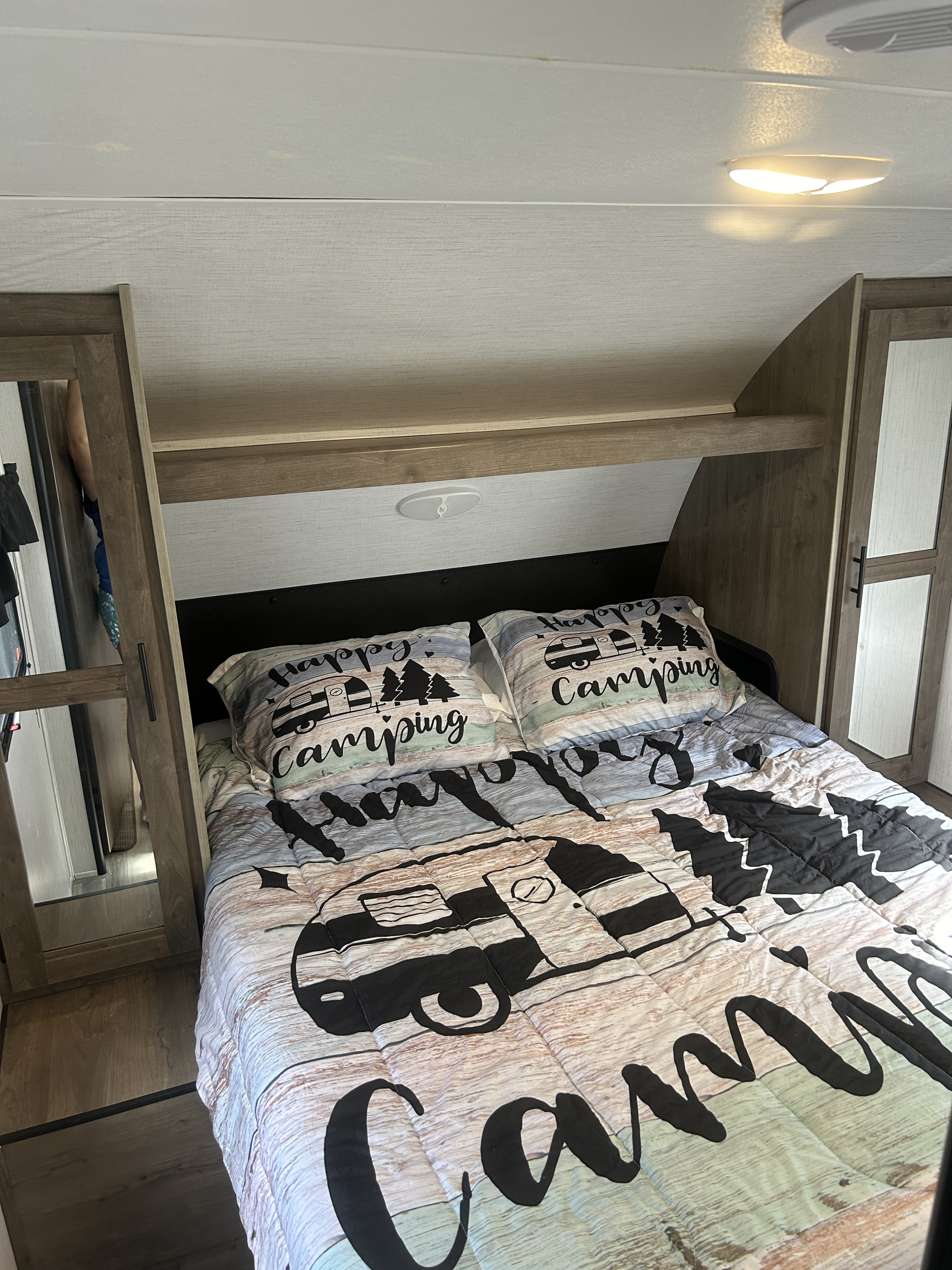 RV rental bedroom featuring a bed with 'Happy Camping' bedding, built-in cabinets, and overhead shelving.. Heartland RVs Pioneer 2023