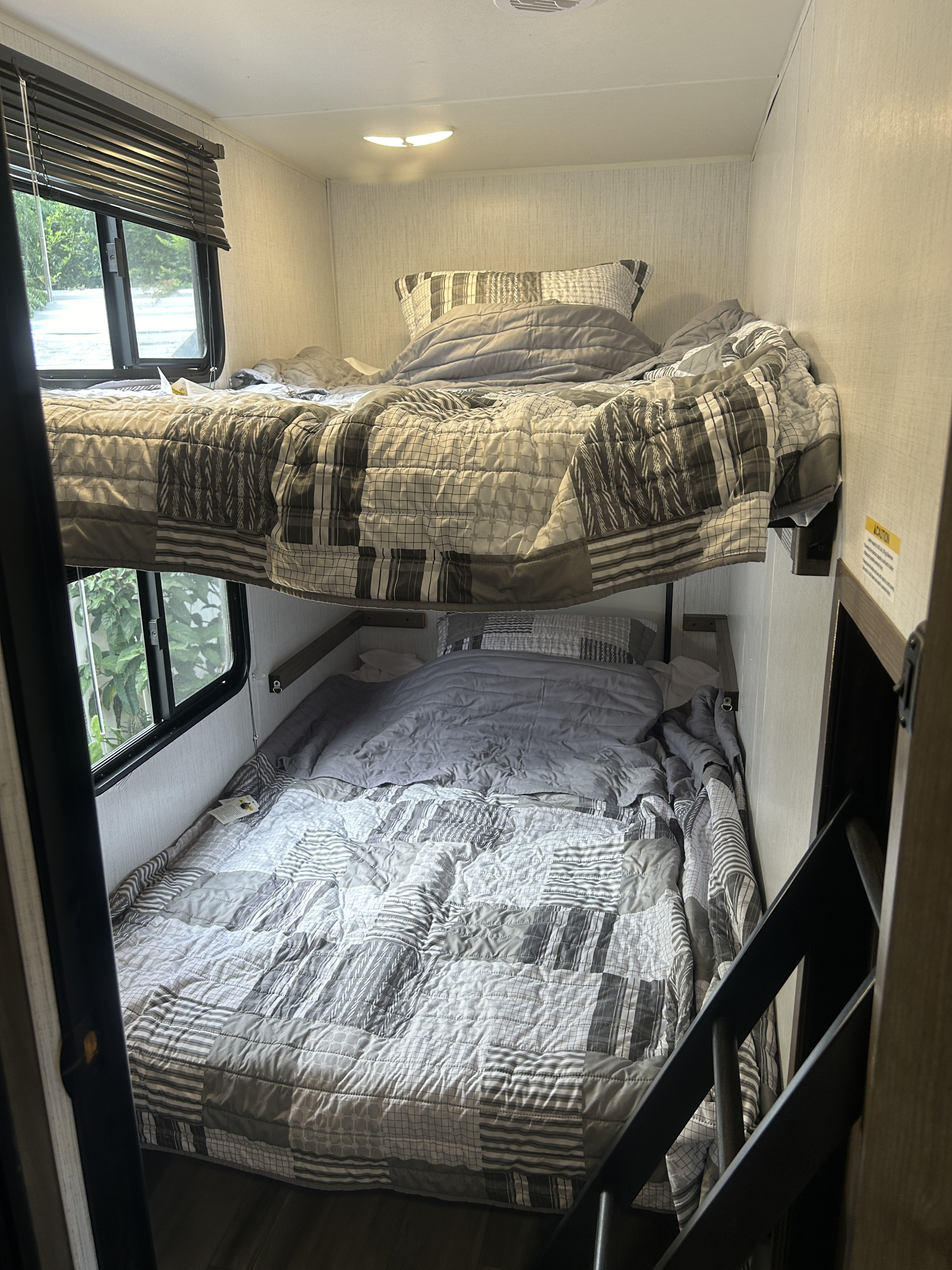 Two comfortable bunk beds with gray patterned quilts and pillows inside an RV rental, offering a relaxing window view.. Heartland RVs Pioneer 2023