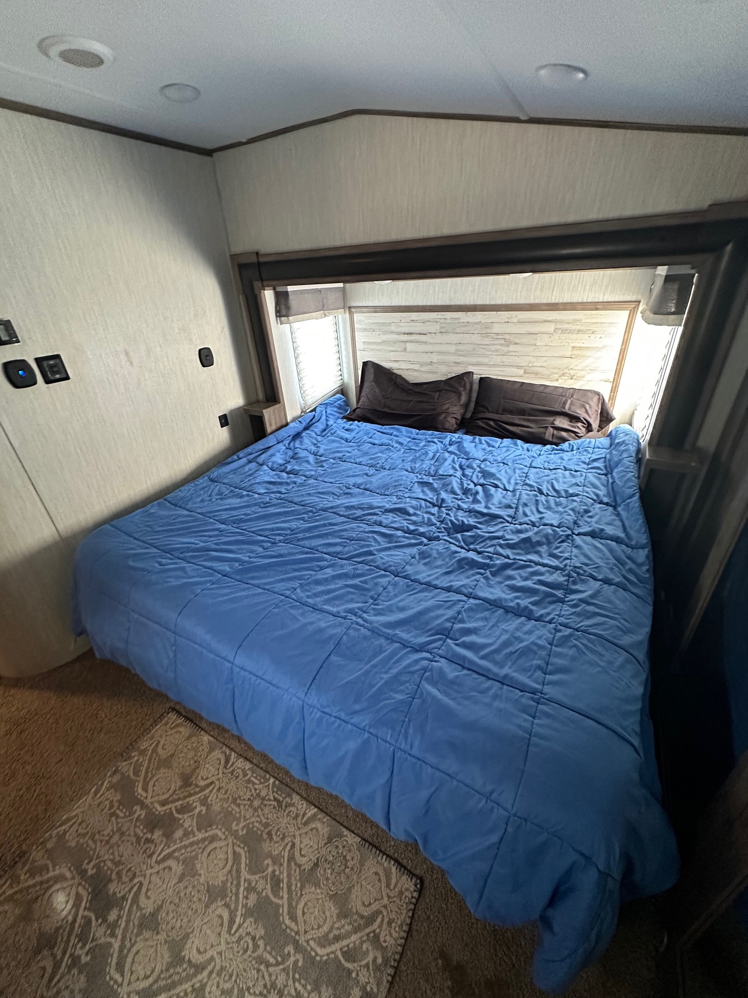 Inside an RV rental, discover a cozy bedroom with a blue bed, dark pillows, and patterned rug.. Forest River Sabre 2019