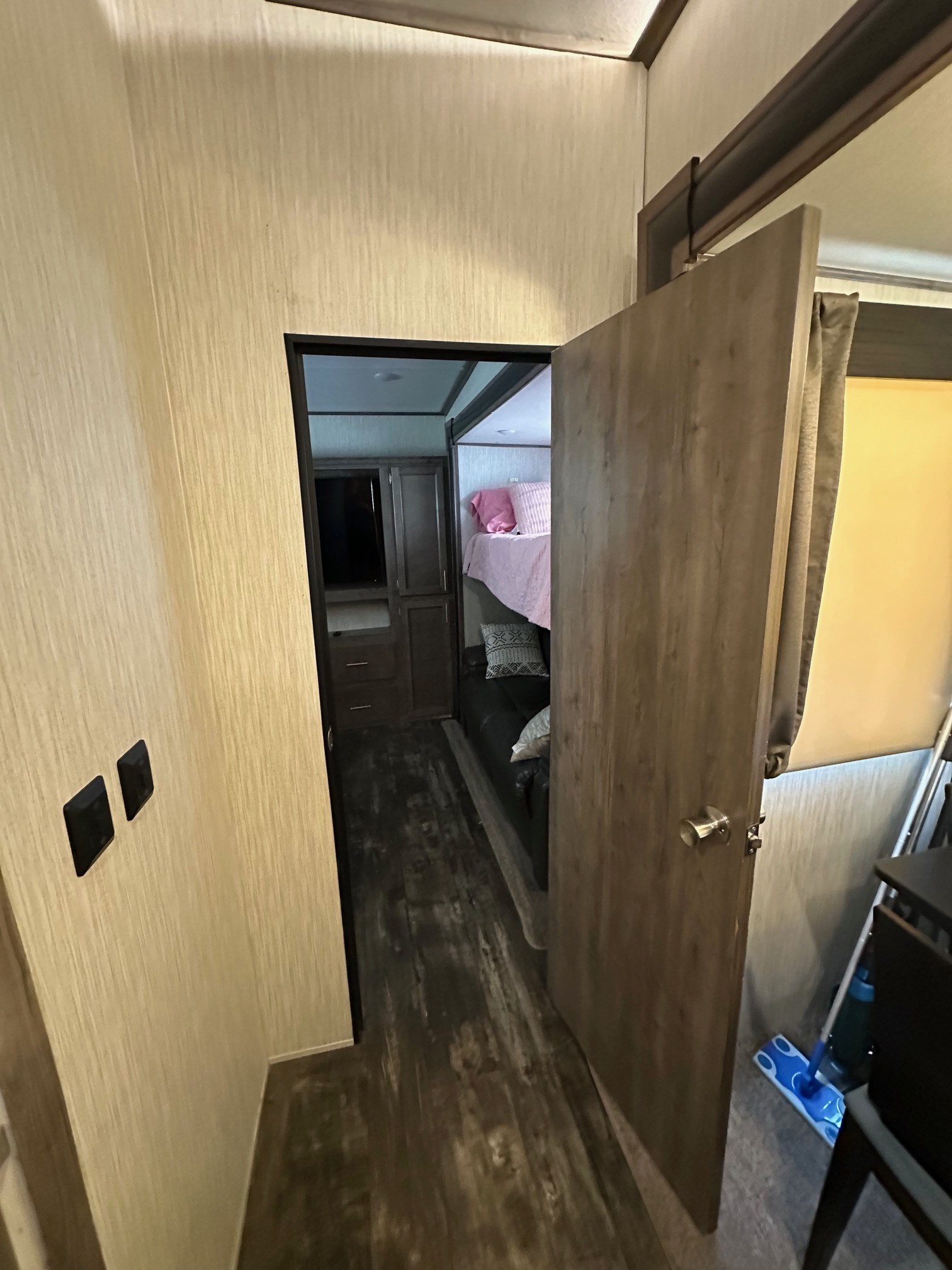 This RV rental interior shows a hallway with light switches, an open door, and a glimpse of bunk beds and built-in storage beyond.. Forest River Sabre 2019