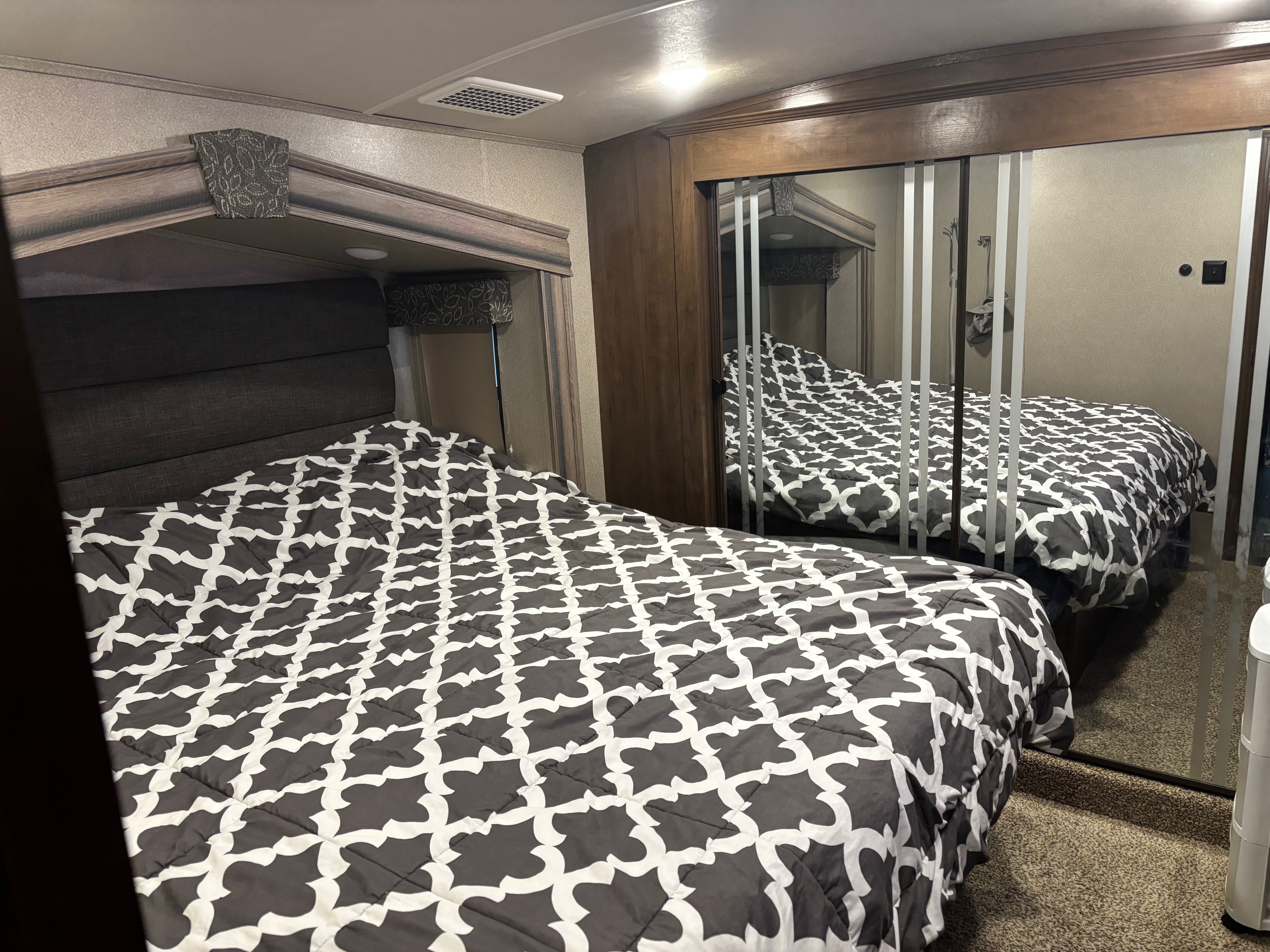Cozy RV rental bedroom with a patterned comforter, padded headboard, and mirrored closet. Perfect for travel adventures.. Cedar Creek Silverback 2018