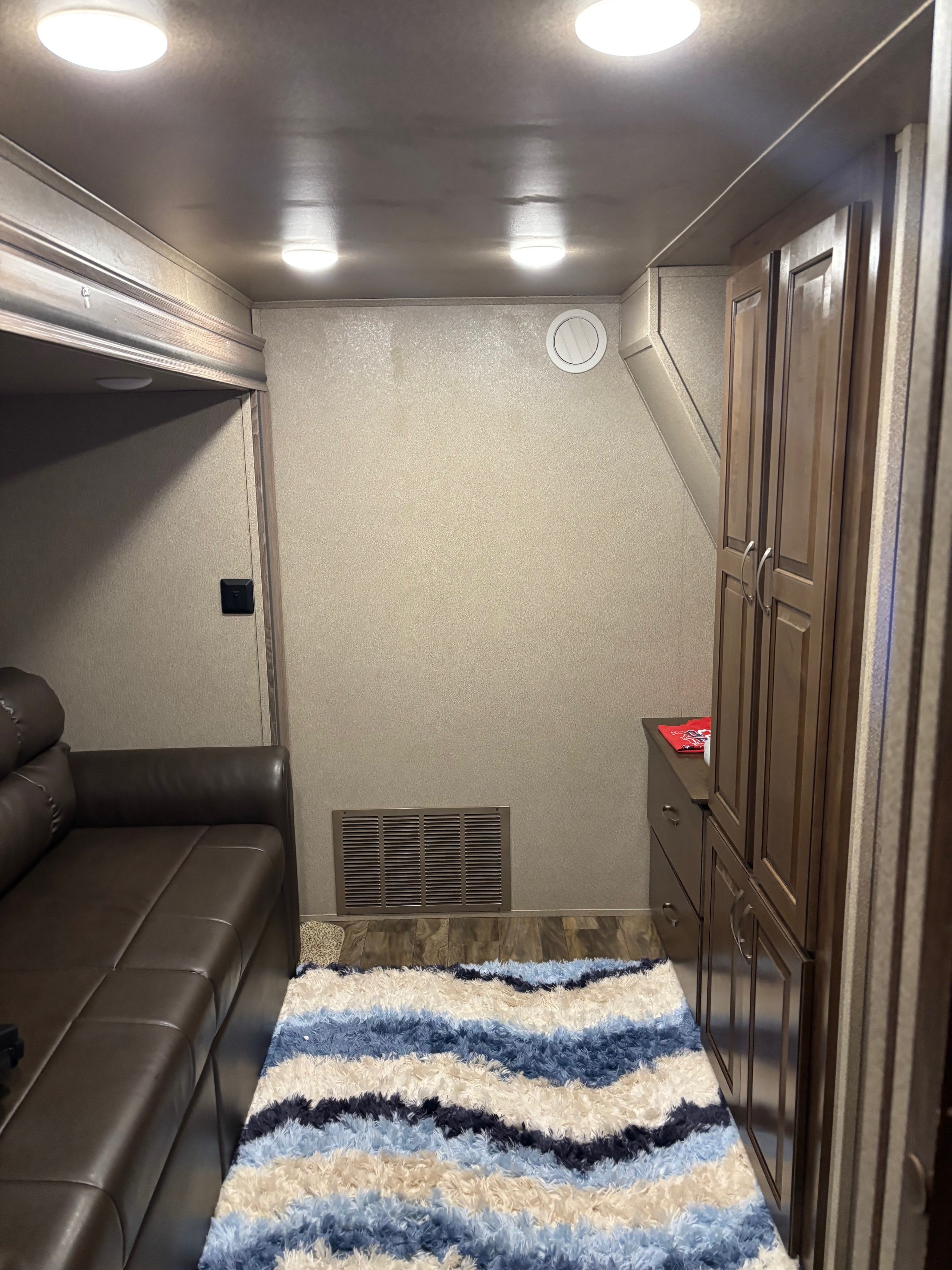 Cozy RV rental living space with a brown leather couch, dark wood cabinets, and a vibrant blue, white, and beige striped rug.. Cedar Creek Silverback 2018