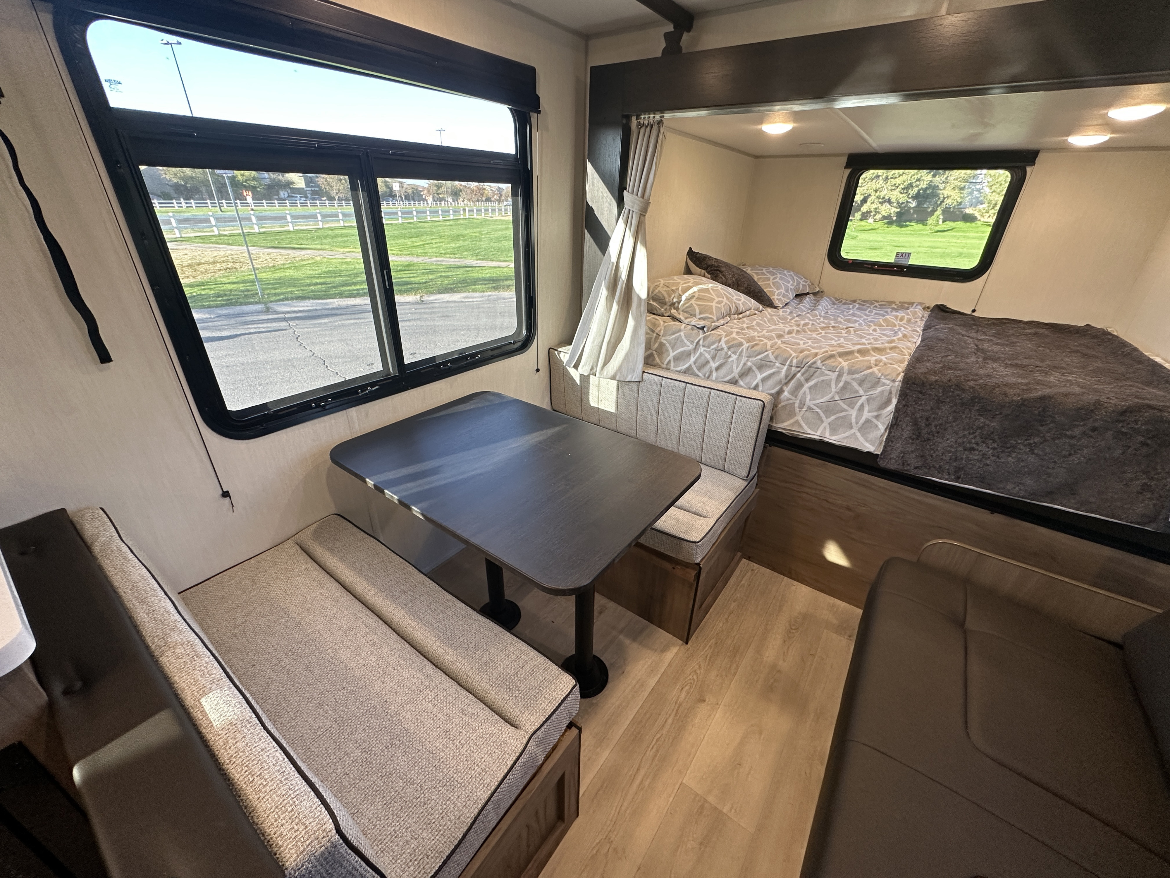 RV rental interior: dinette on left, bed on right, with large windows revealing outdoor scenery.. Forest River Cherokee 2025
