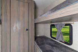 Inside an RV rental: a wooden cabinet, window with tied grey curtains, and bunk beds for extra sleeping space.. Gulf Stream Kingsport 2022