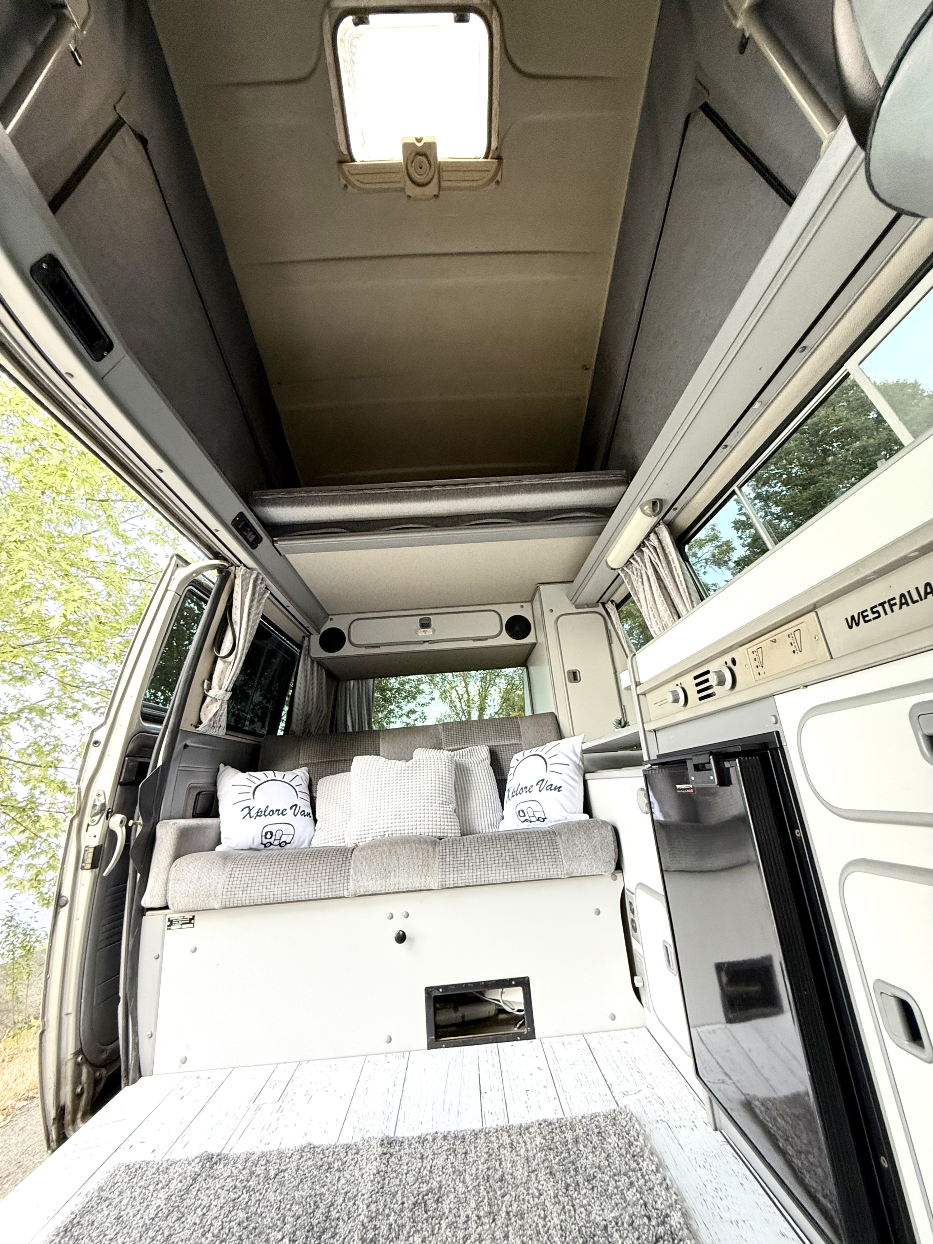 Interior of a Westfalia RV rental featuring a cozy bed, pop-top, and compact kitchen. Ready for adventures!. Volkswagen T3 Westfalia 1989