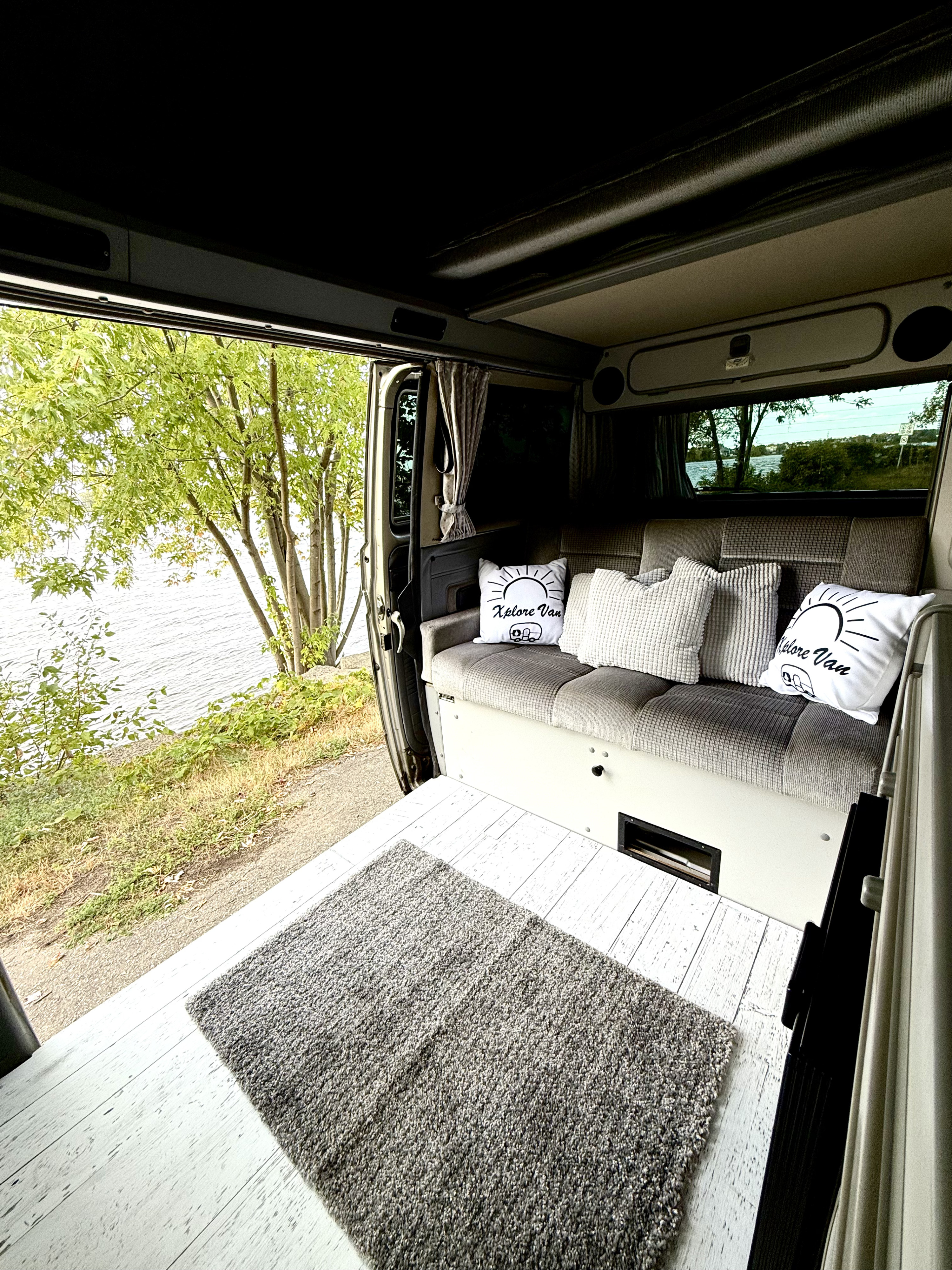 Inviting RV rental offers a cozy interior with plush cushions and a beautiful lake view from the open side door.. Volkswagen T3 Westfalia 1989