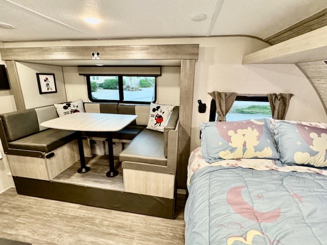 Cozy Disney-themed RV rental interior featuring a spacious dinette with Mickey pillows and a comfortable bed.. Forest river Aurora 2025