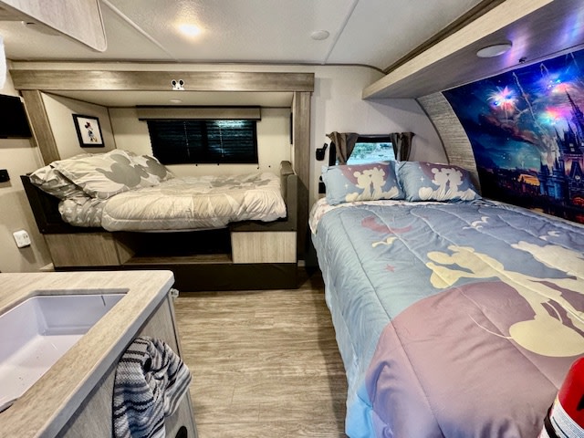 Inside an RV rental with two cozy, Disney-themed beds: one Mickey, one Lilo & Stitch with castle mural.. Forest river Aurora 2025