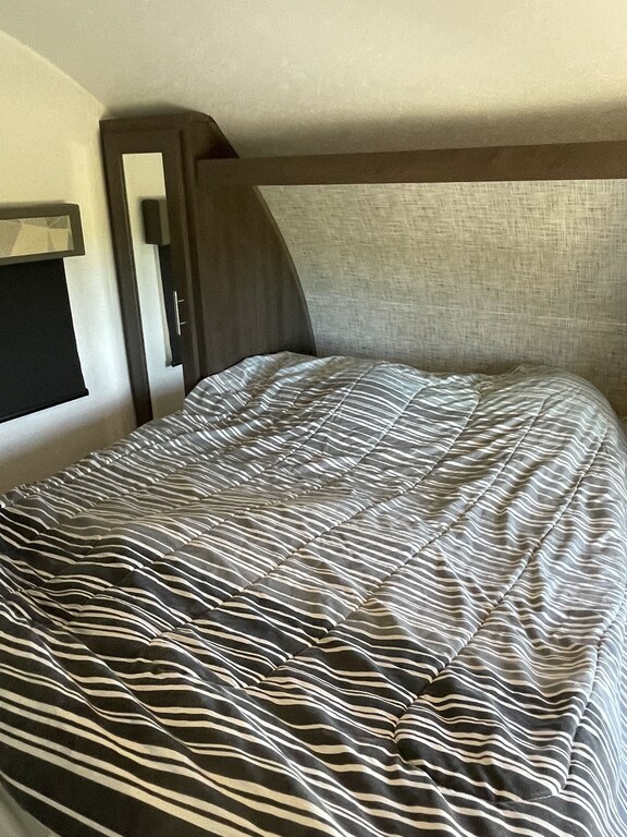View of an RV rental's cozy bedroom featuring a neatly made striped bed and built-in bedside storage.. Forest River Salem Cruise Lite 2019