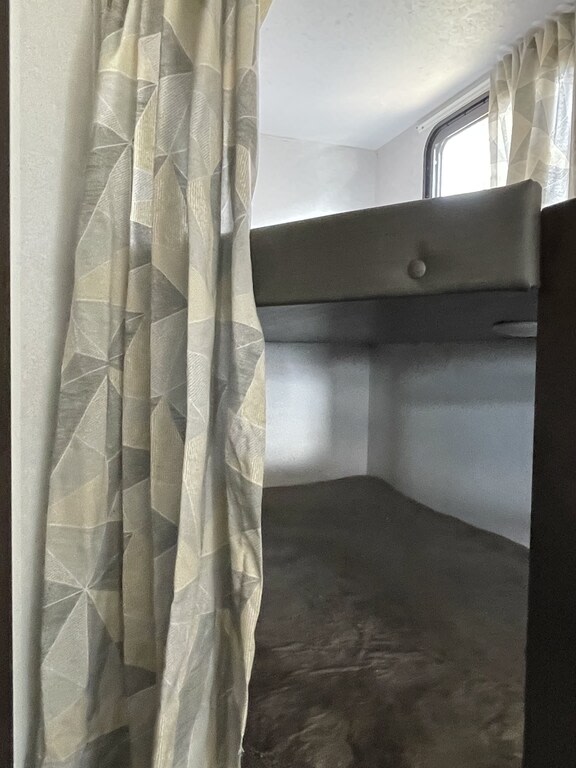 Inside an RV rental, a set of bunk beds awaits. A patterned curtain hangs left, a window provides light above the dark top bunk.. Forest River Salem Cruise Lite 2019