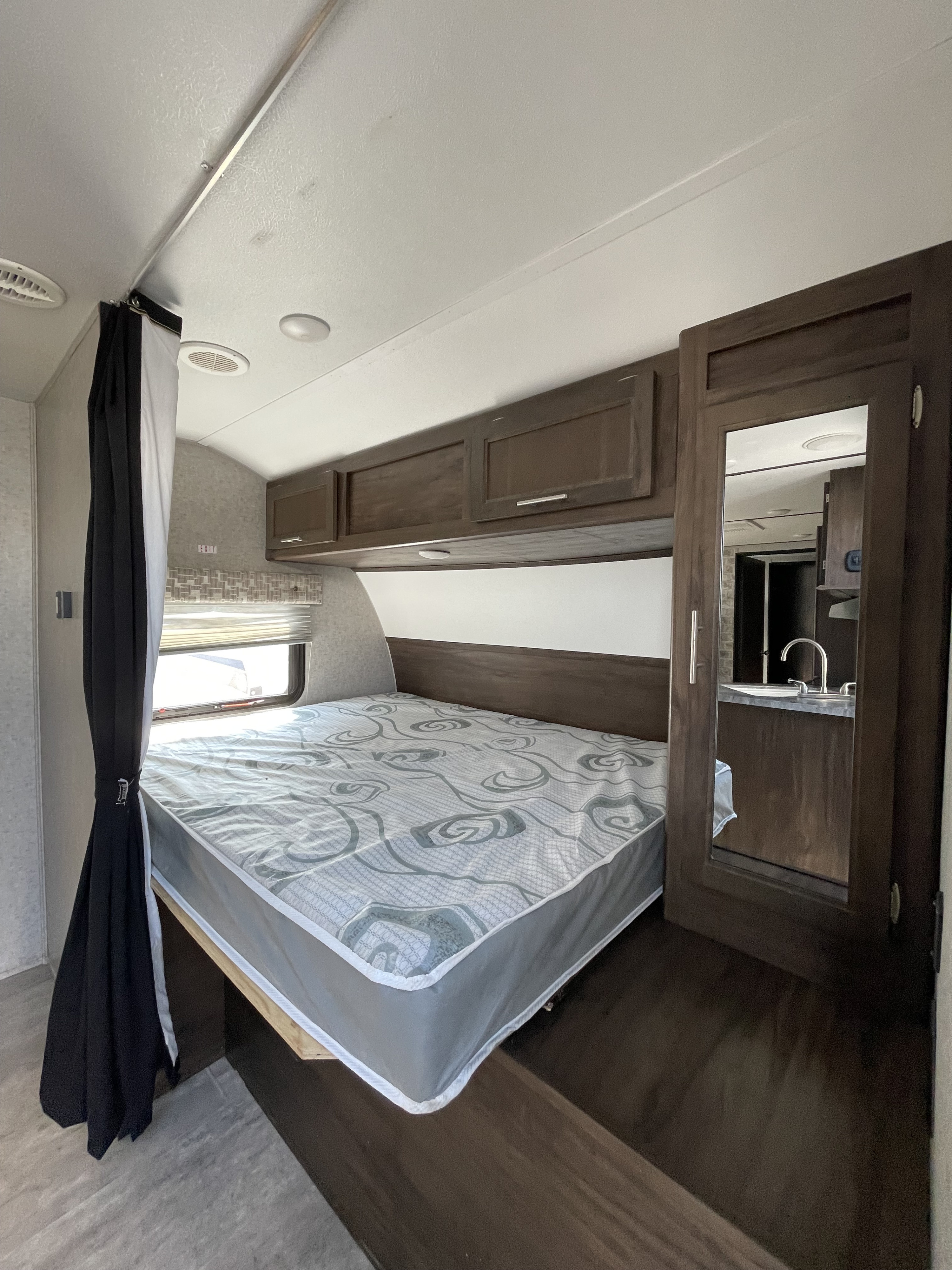Inside an RV rental, discover a compact bedroom featuring a bed, overhead cabinets, and a mirrored door.. Forest River Nitro Xlr 2020