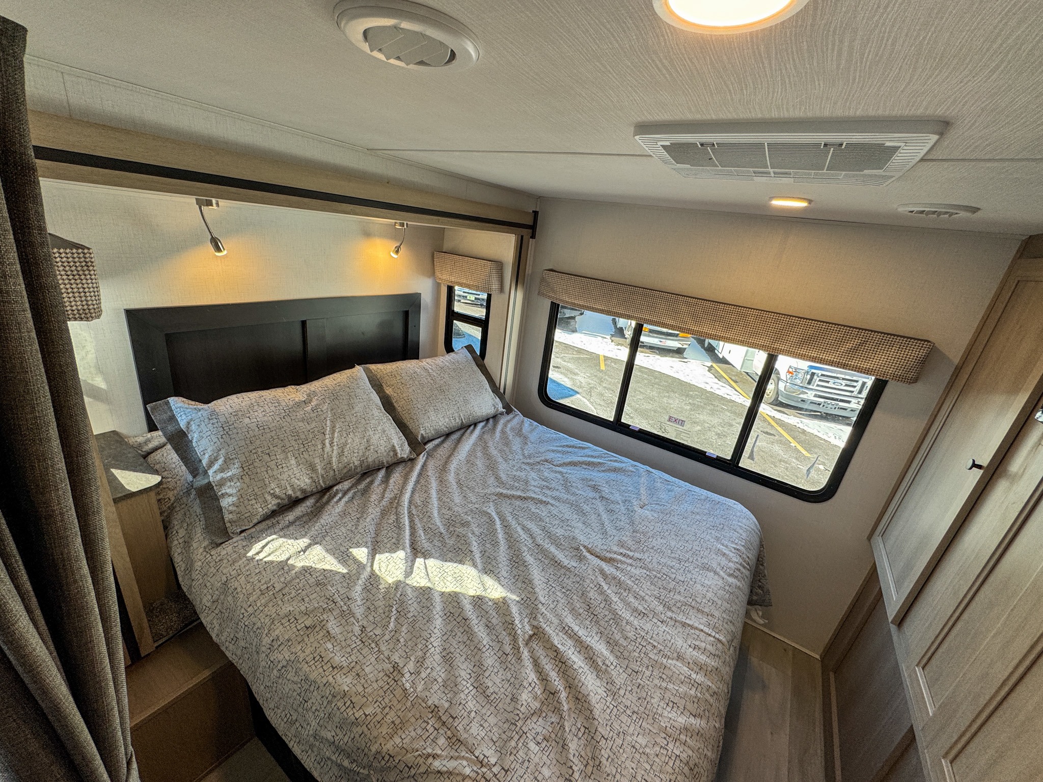 Step into this RV rental bedroom, featuring a patterned bed, windows with shades, overhead lighting, and AC unit.. Forest River Sunseeker 2025