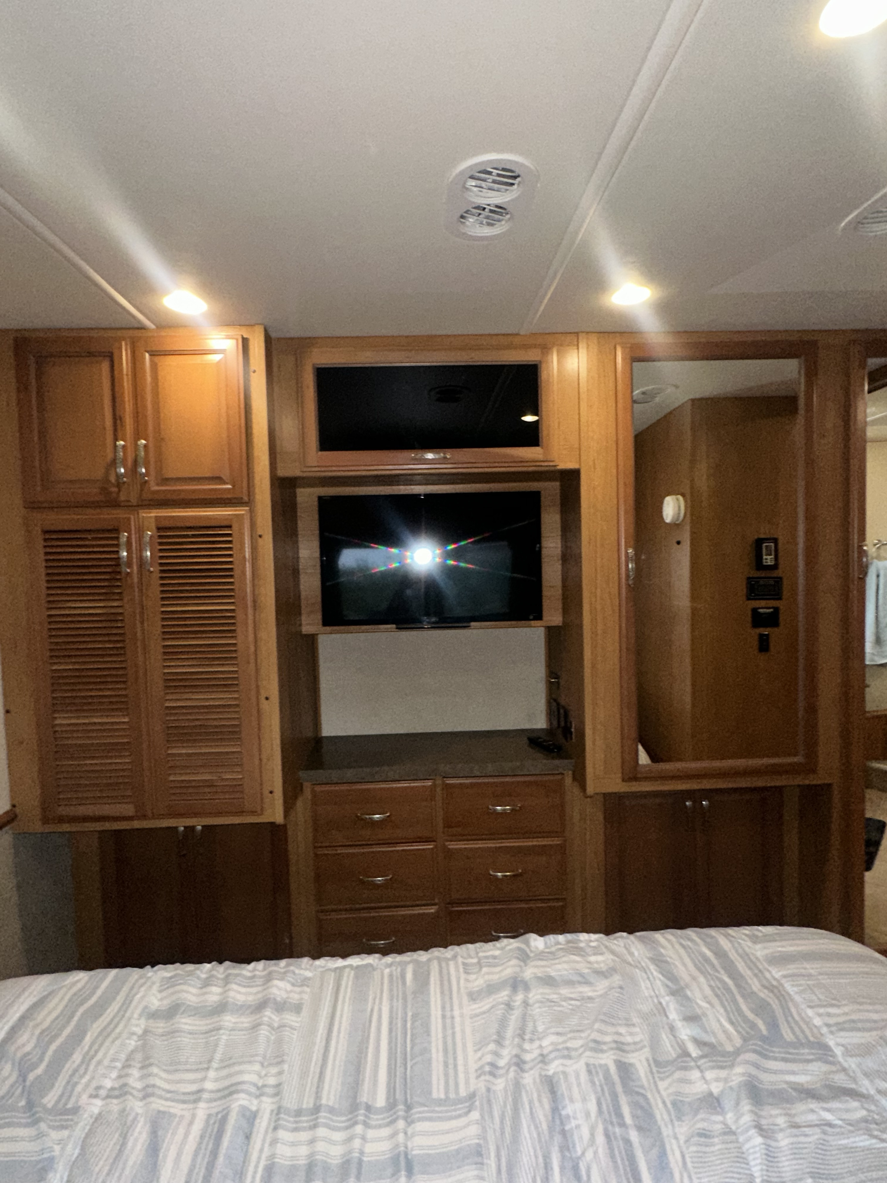 Cozy RV rental bedroom interior with built-in wood cabinetry, TV, ample storage, and a striped bed.. Fleetwood Bounder 33C 2015