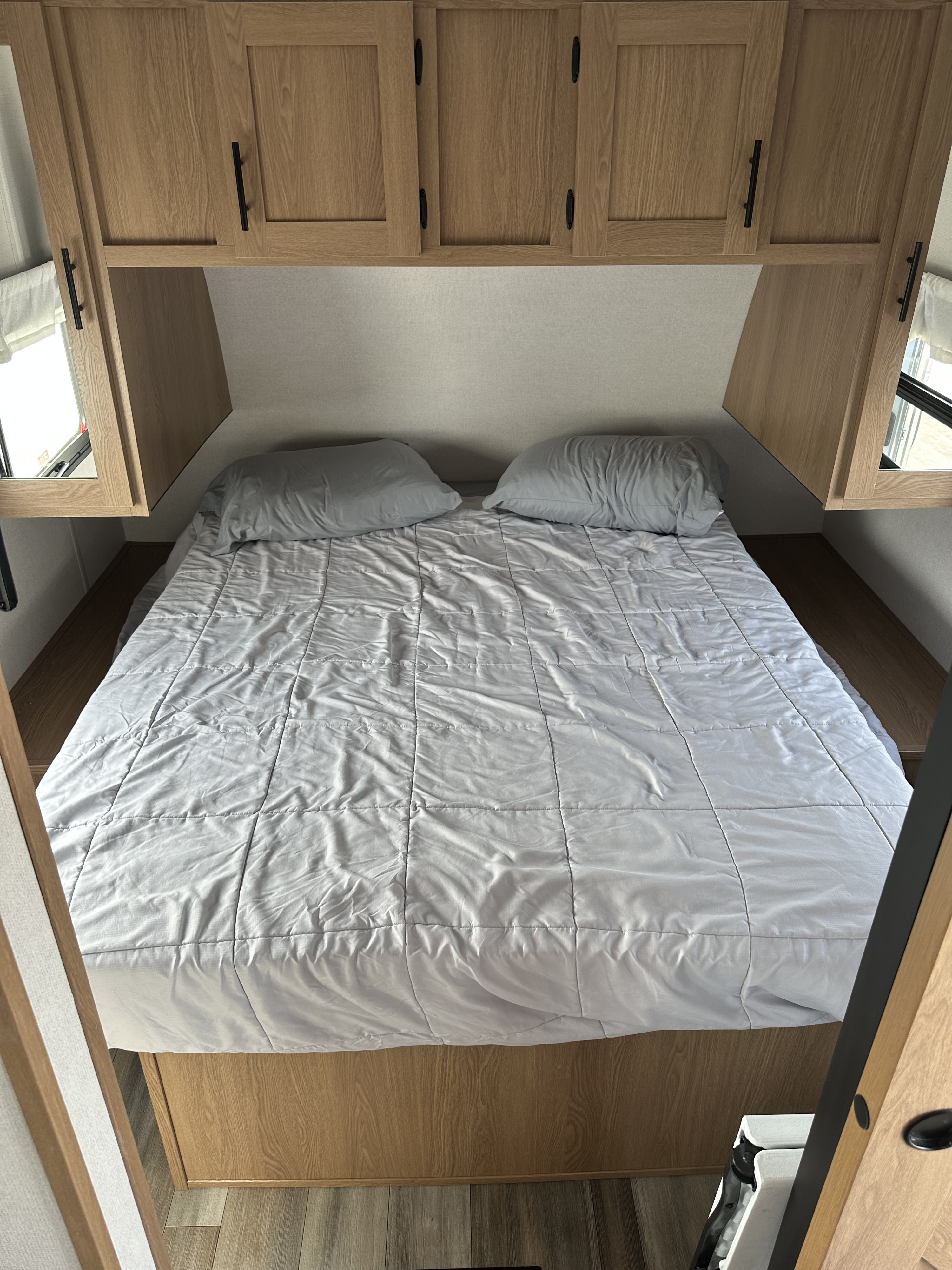 RV rental interior: A cozy bedroom with a light grey bed, overhead wooden cabinets, and side shelves.. Avenger Avenger Trailer 2022
