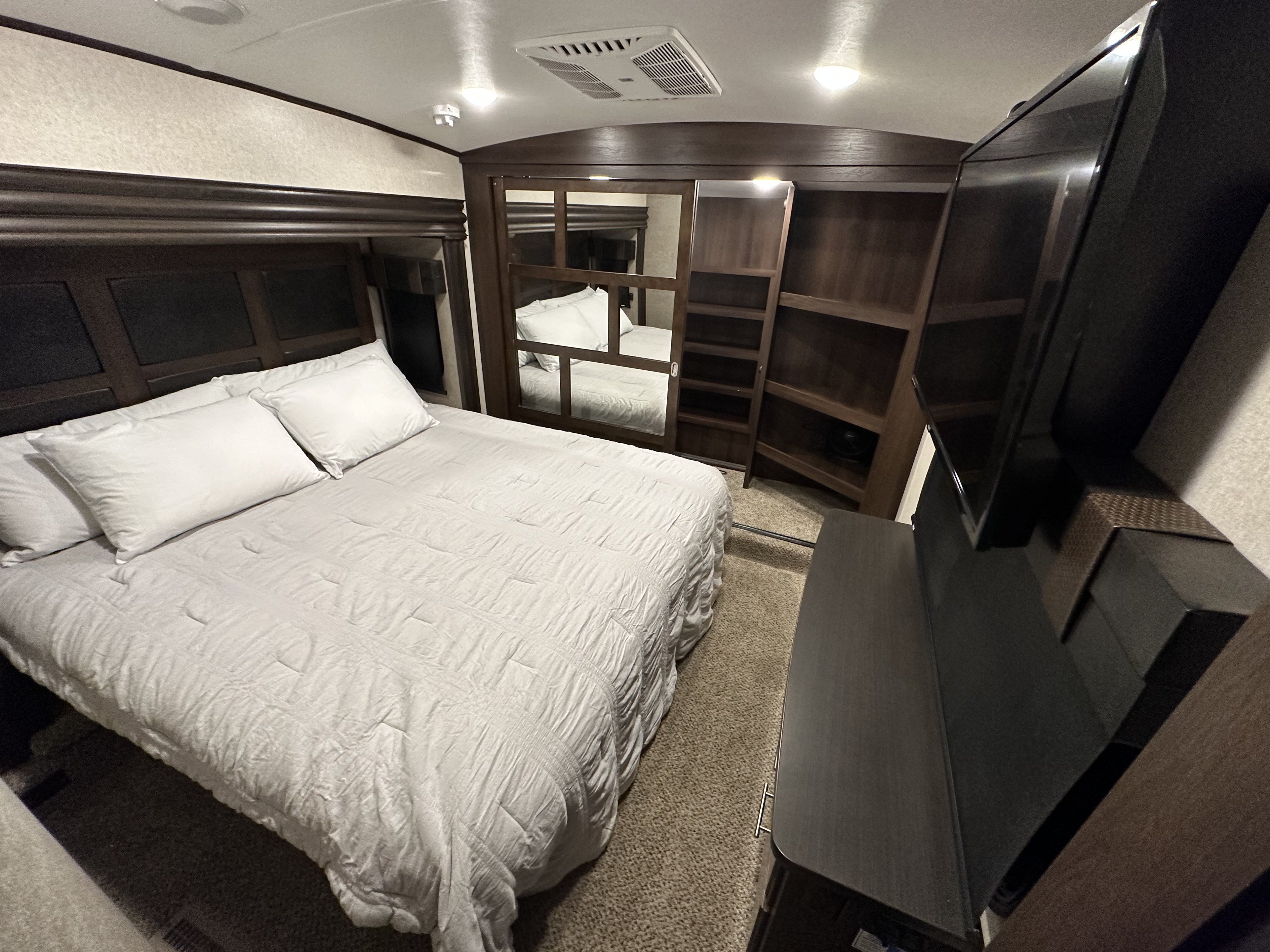 Cozy RV rental bedroom with a comfy bed, wall-mounted TV, and dark wood built-in storage.. Jayco North Point 2018