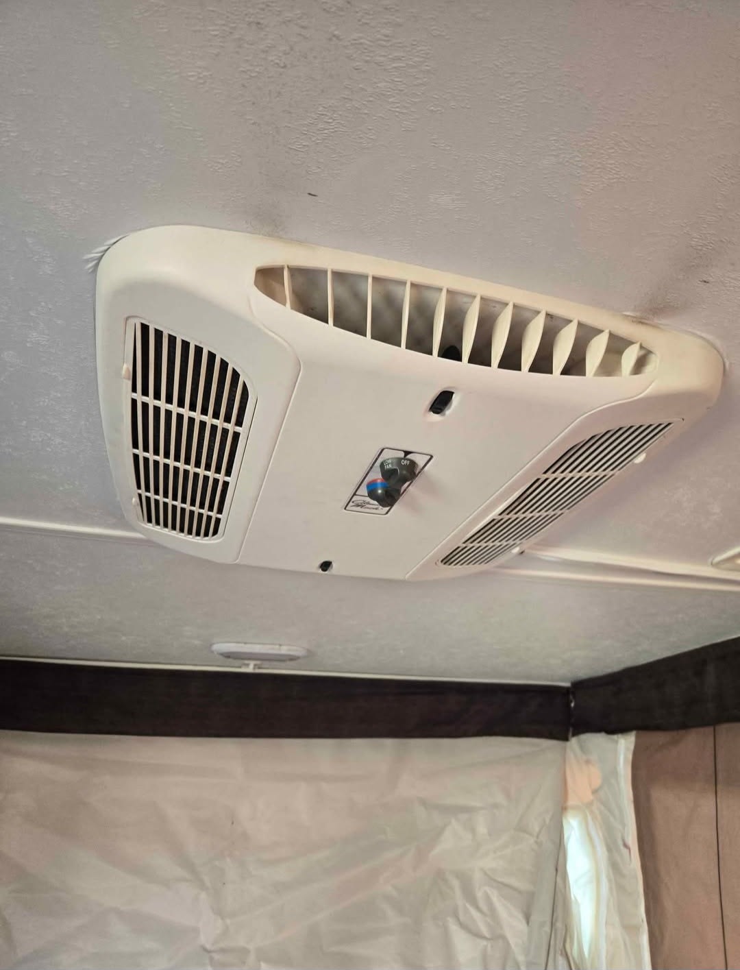 Inside an RV rental: A white ceiling-mounted AC unit is prominent, with the textured ceiling & fabric sleeping area visible.. Coachmen Clip M128 2017