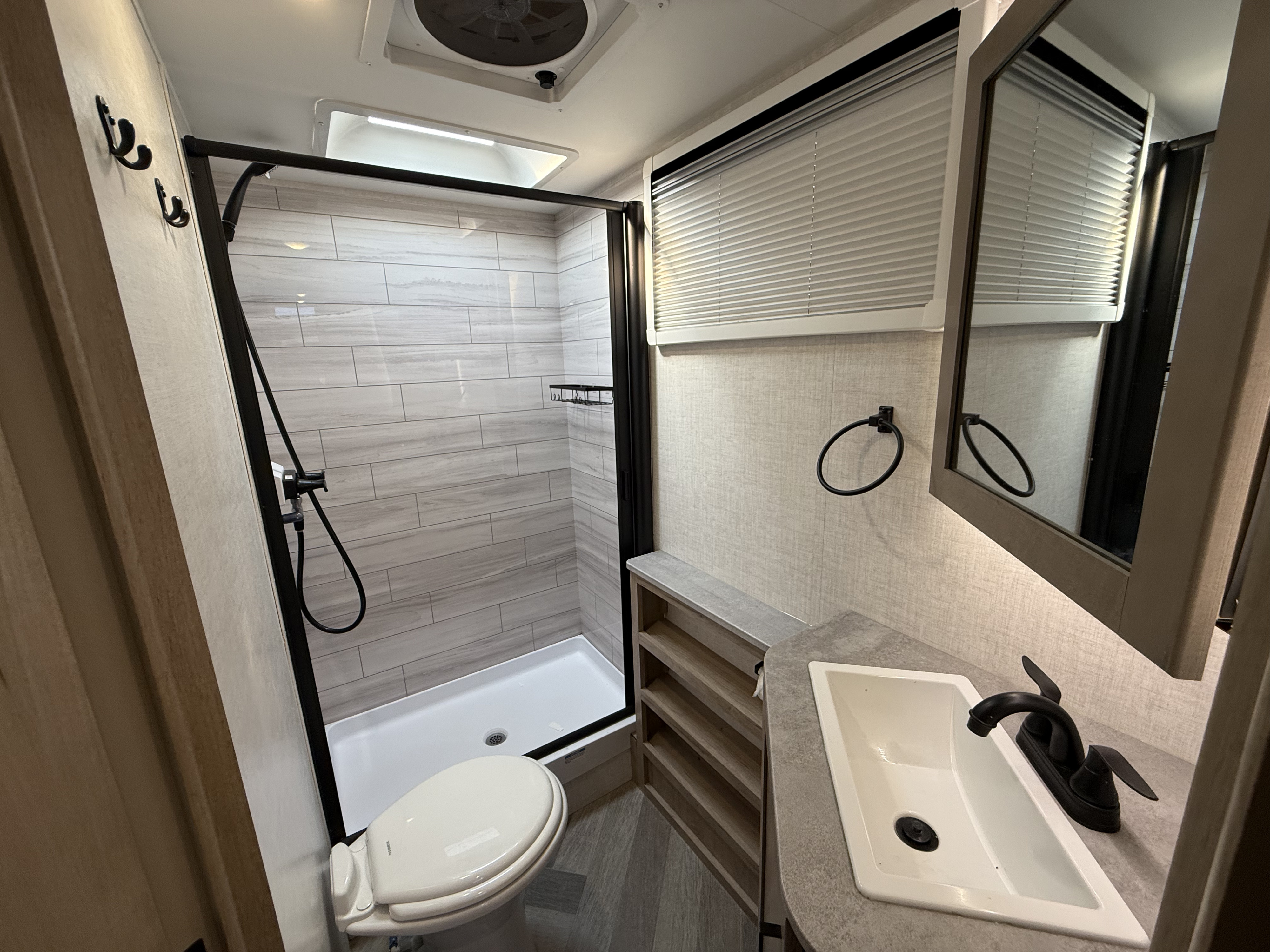 Clean camper bathroom with shower, toilet, sink, and storage
