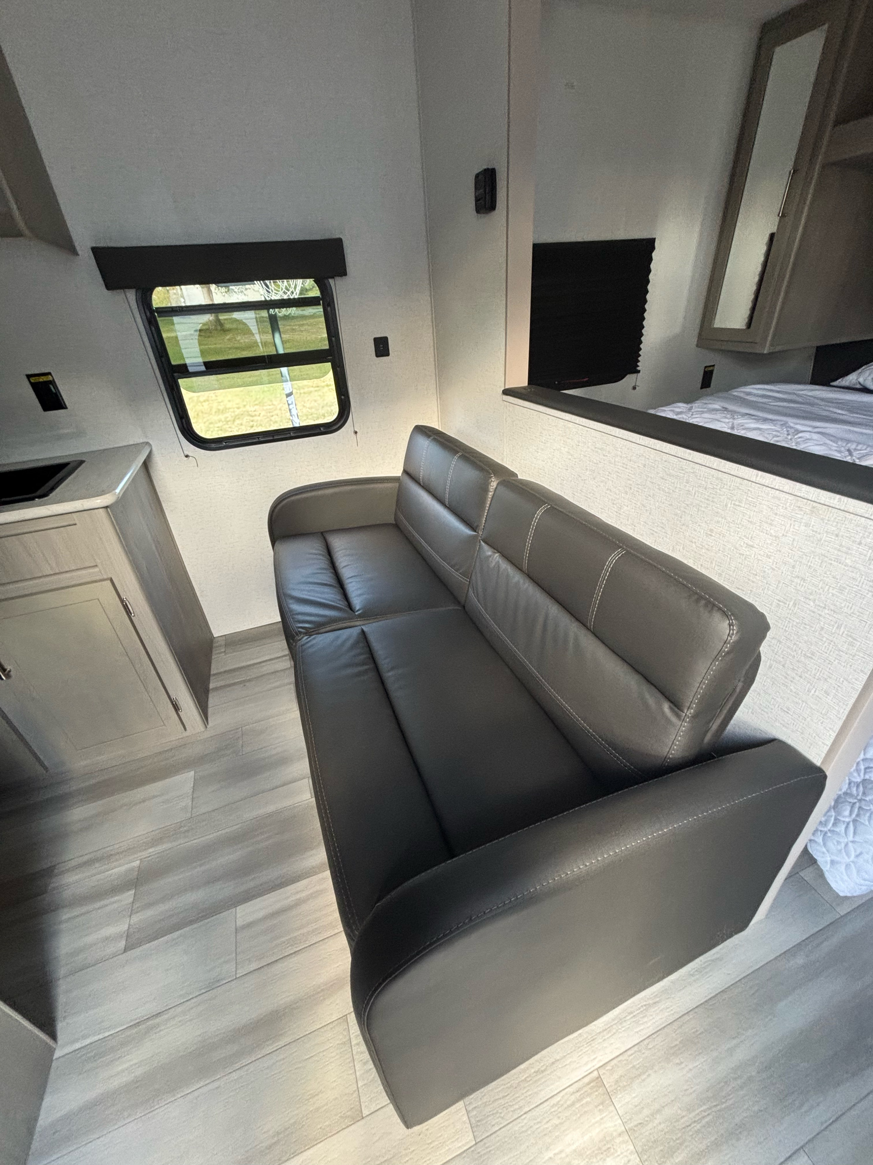 Inside a modern RV rental: a plush sofa, compact kitchen sink, and cozy sleeping area with a scenic window view.. Keystone RV Classic 2024