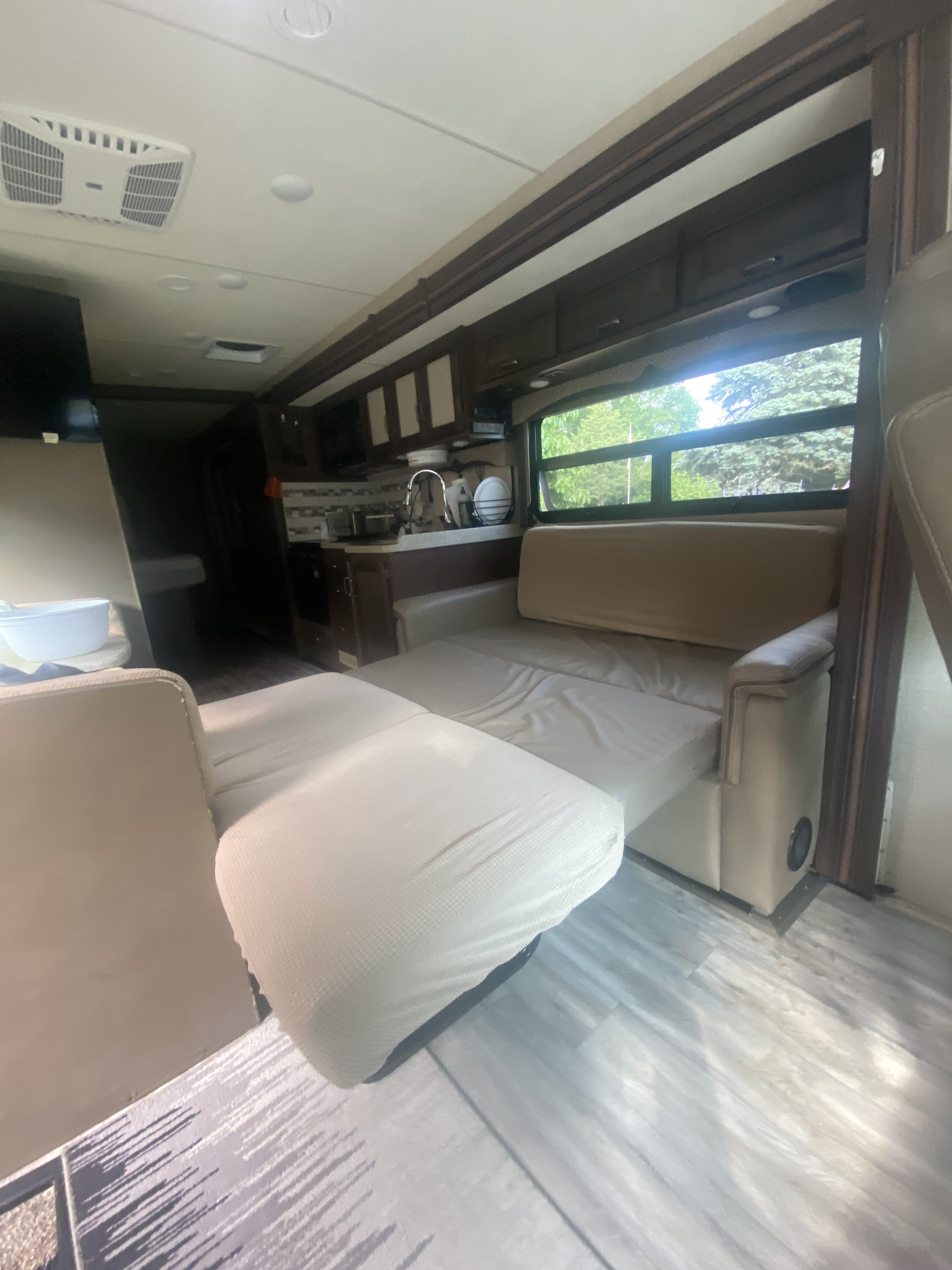 RV rental interior: A light-colored sofa bed extends into the living area, with a full kitchen and window showing trees.. Thor Hurricane 2018