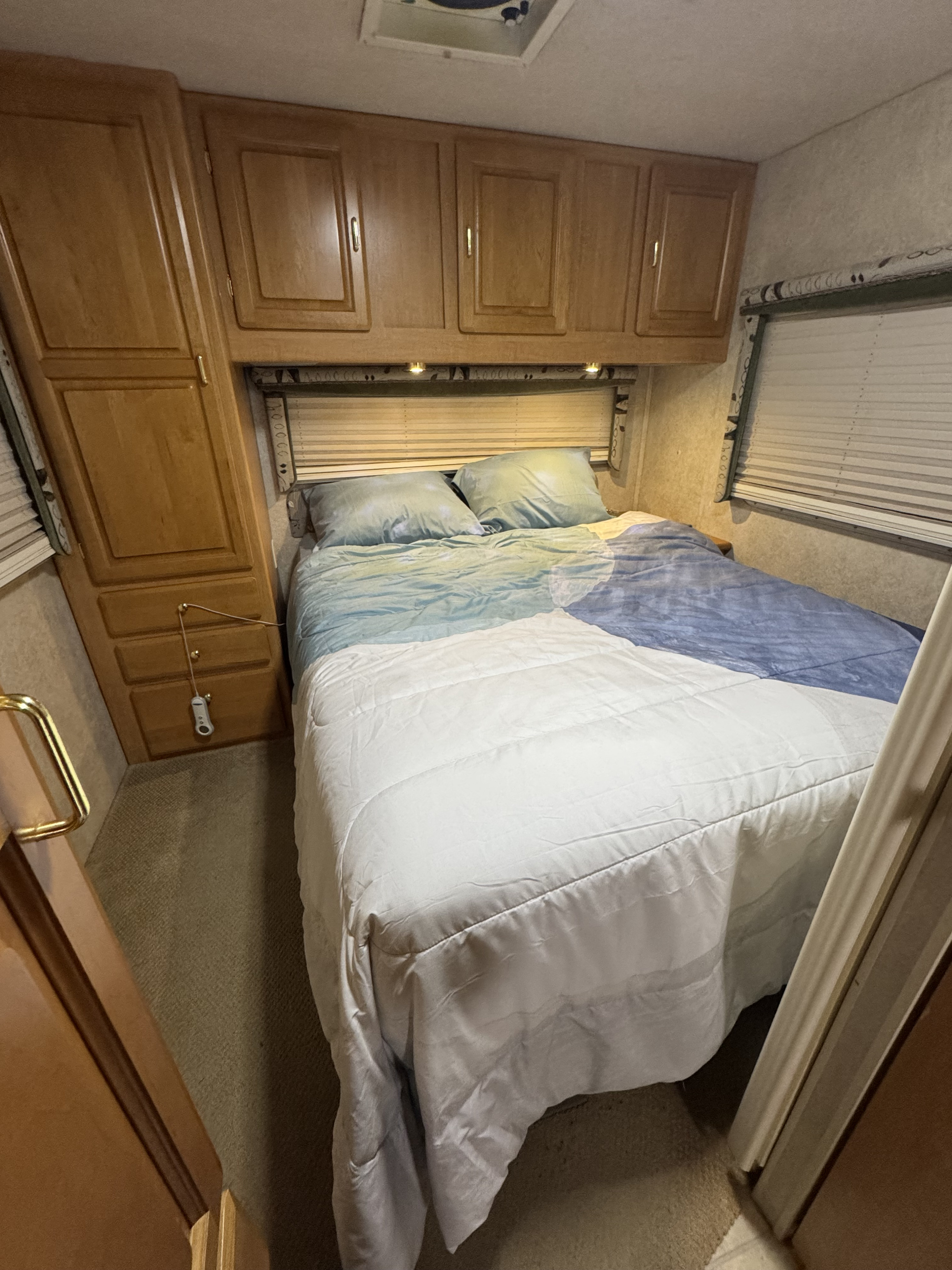 Cozy RV rental bedroom: wooden cabinets, comfortable bed with blue/white bedding, and window blinds.. Jayco Granite Ridge 2003