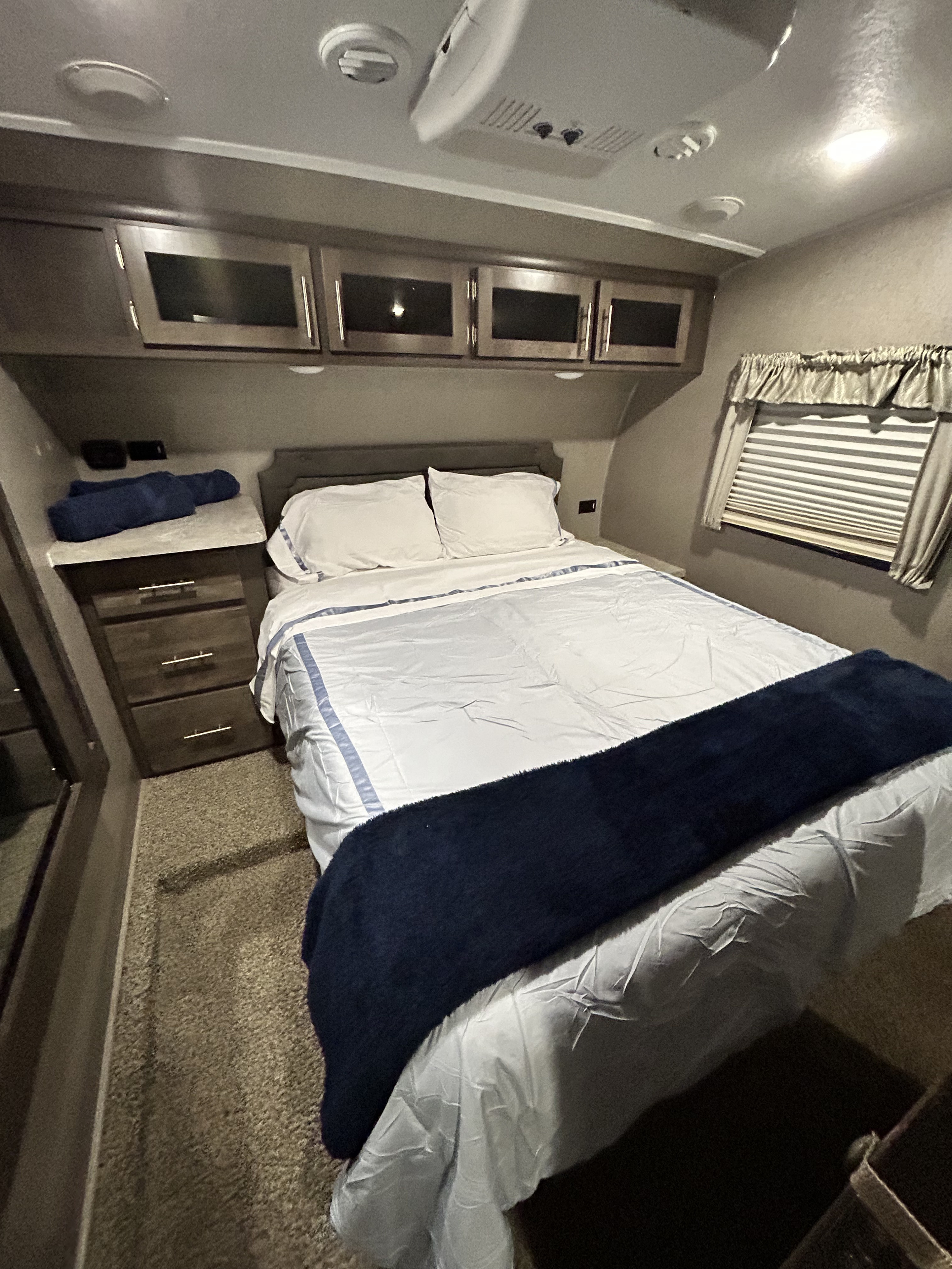 This RV rental's cozy bedroom features a bed with white and blue linens, overhead storage, and a window.. Forest River Flagstaff Super Lite 2019