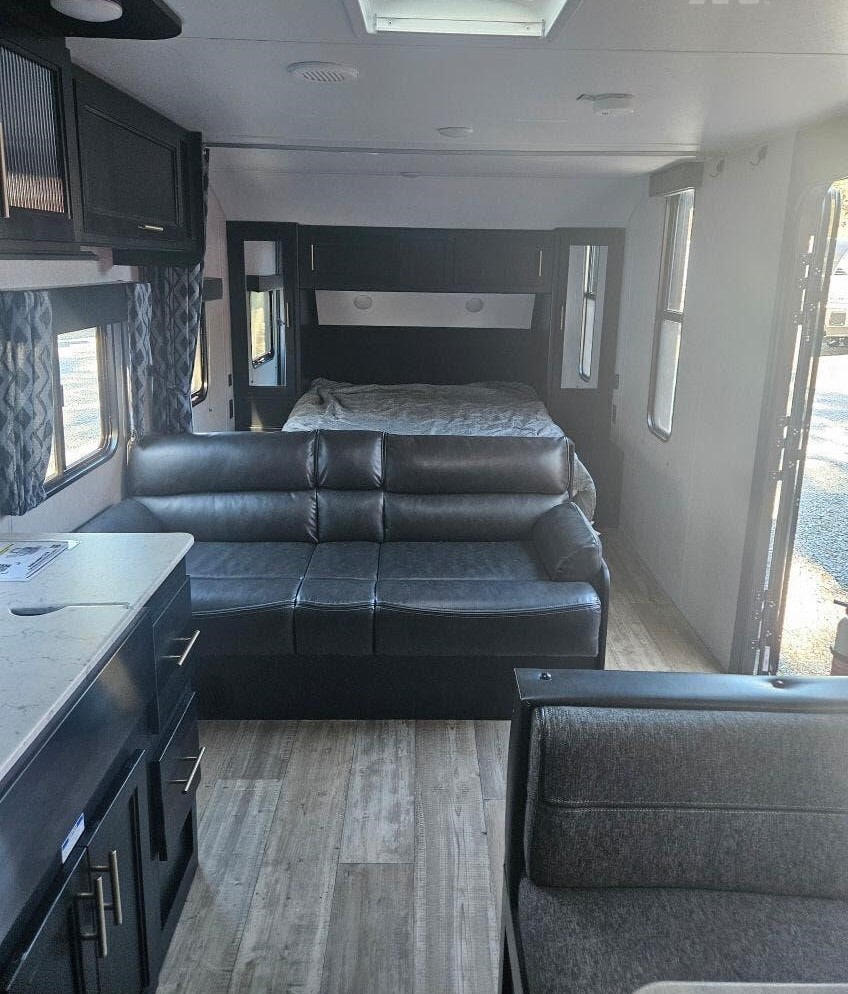 Spacious RV rental interior with a black sofa, bed, kitchen, and dinette. Ideal travel trailer living space.. Forest River Cherokee Grey Wolf 2022