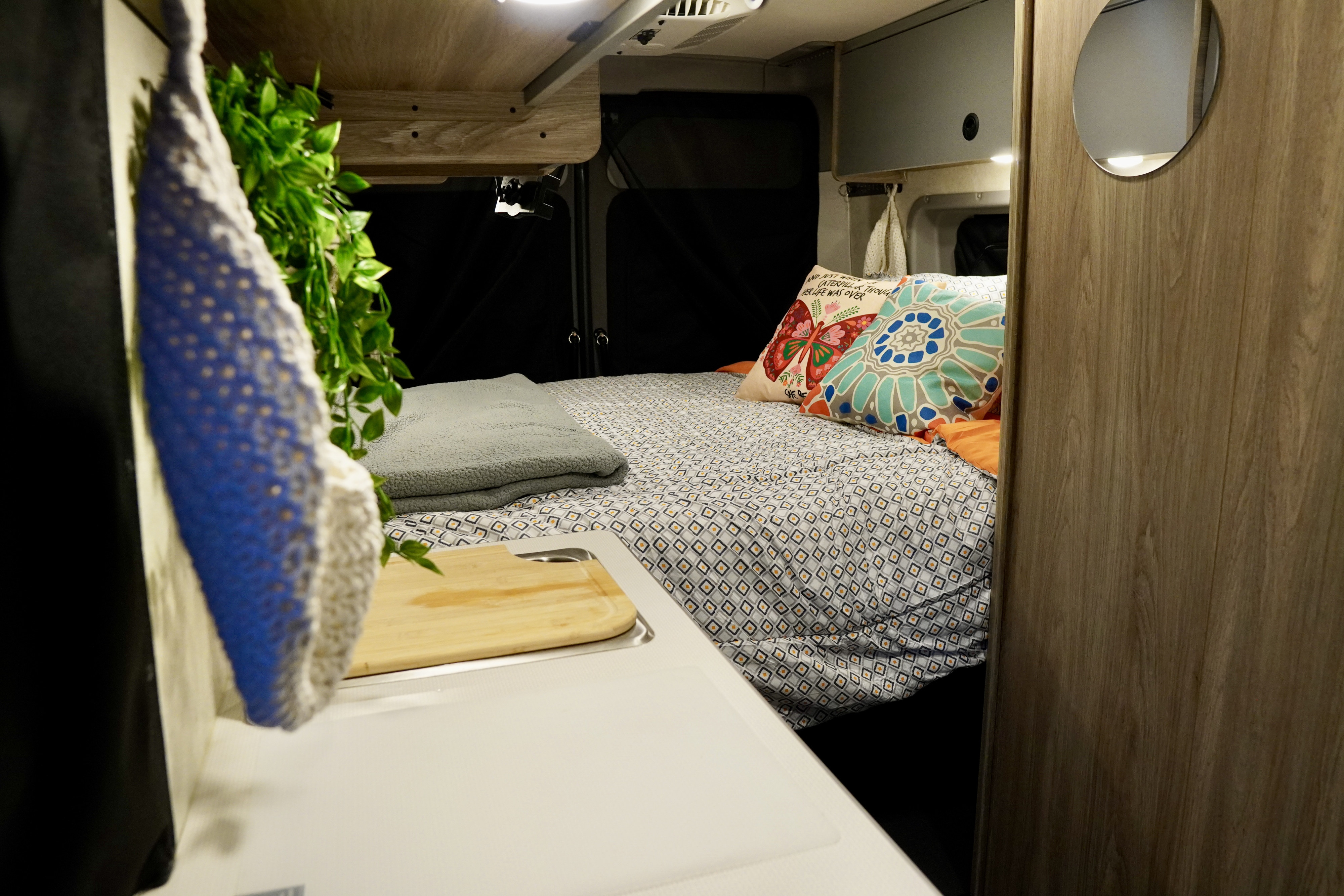 Cozy RV rental interior with a patterned bed, colorful pillows, and a compact kitchen area with a sink.. Winnebago Solis 59PX 2025