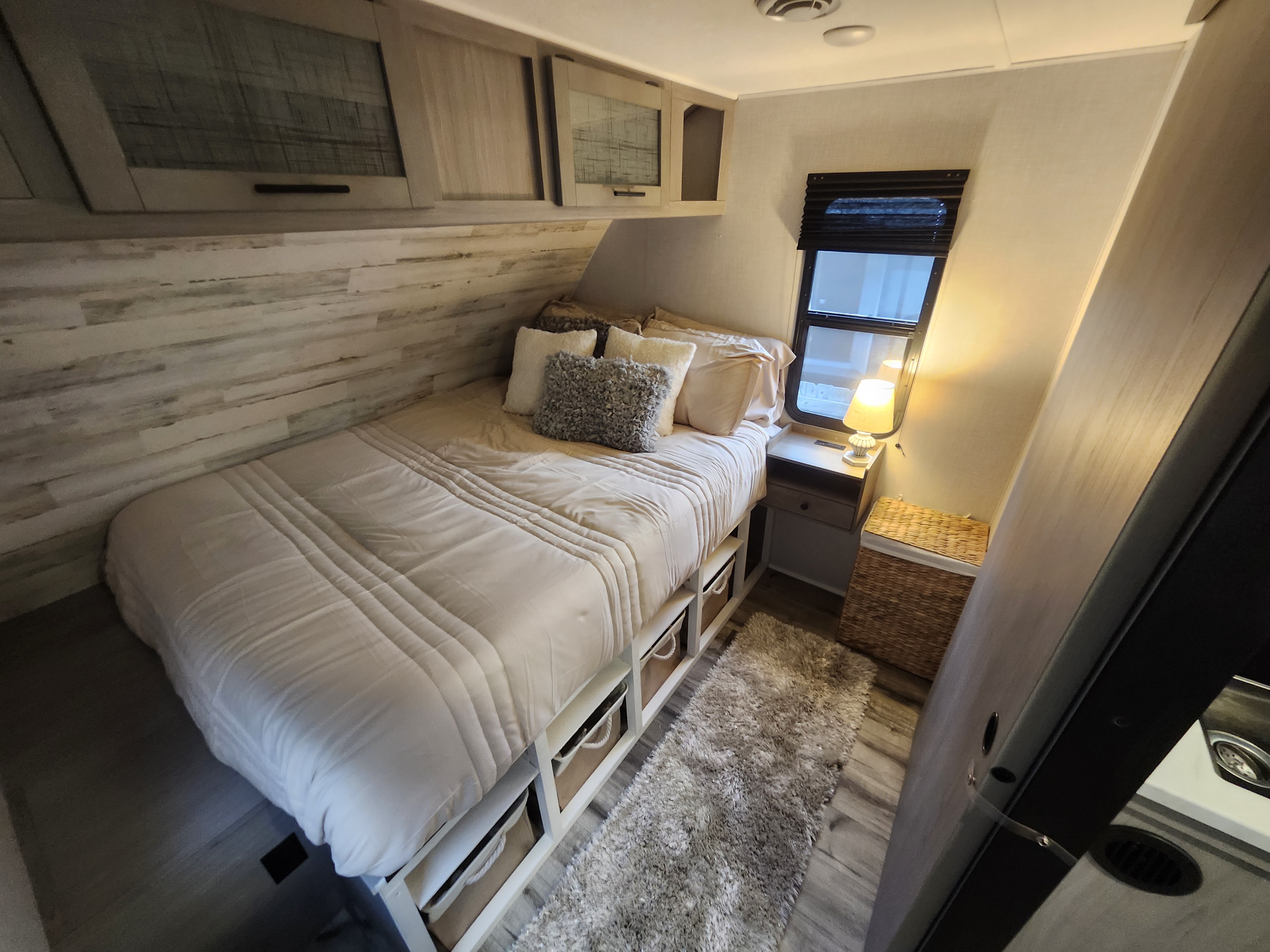 Inside a cozy RV rental bedroom: features a comfortable bed with under-bed storage, built-in cabinets, and warm lighting.. Dutchmen Coleman Lantern 2023