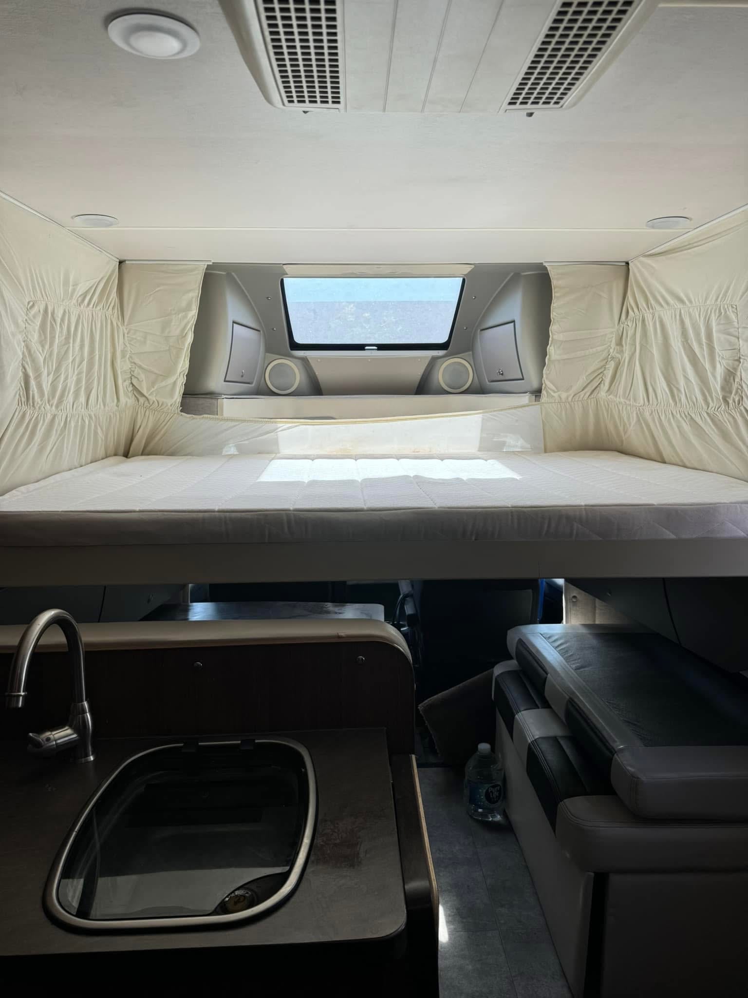 RV rental interior: cozy cab-over bed, compact kitchen sink, and living space visible below. Ideal for trips.. Winnebago Trend 2014