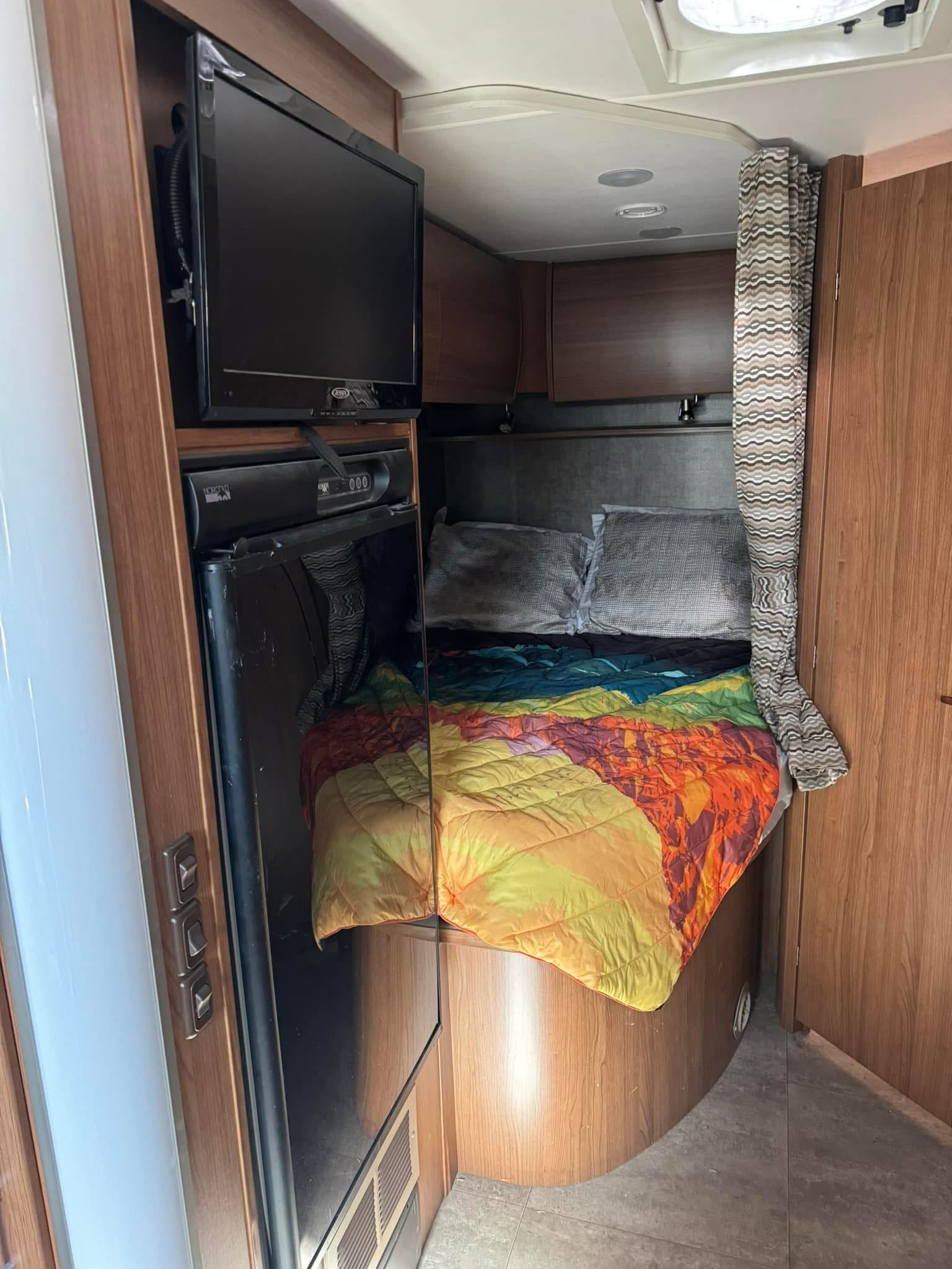 RV rental interior: A cozy bedroom with colorful bedding, wall-mounted TV, and compact refrigerator.. Winnebago Trend 2014