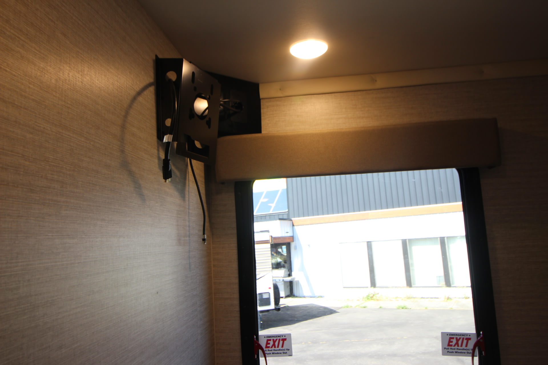 RV rental interior featuring a TV mount, textured wall, window with emergency exit sign, and overhead light.. Winnebago Spirit 26 T 2025