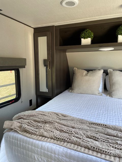 Cozy RV rental bedroom featuring a quilted bed, knit blanket, pillows, and convenient built-in storage with decor.. Grand Design Transcend Xplor 2021