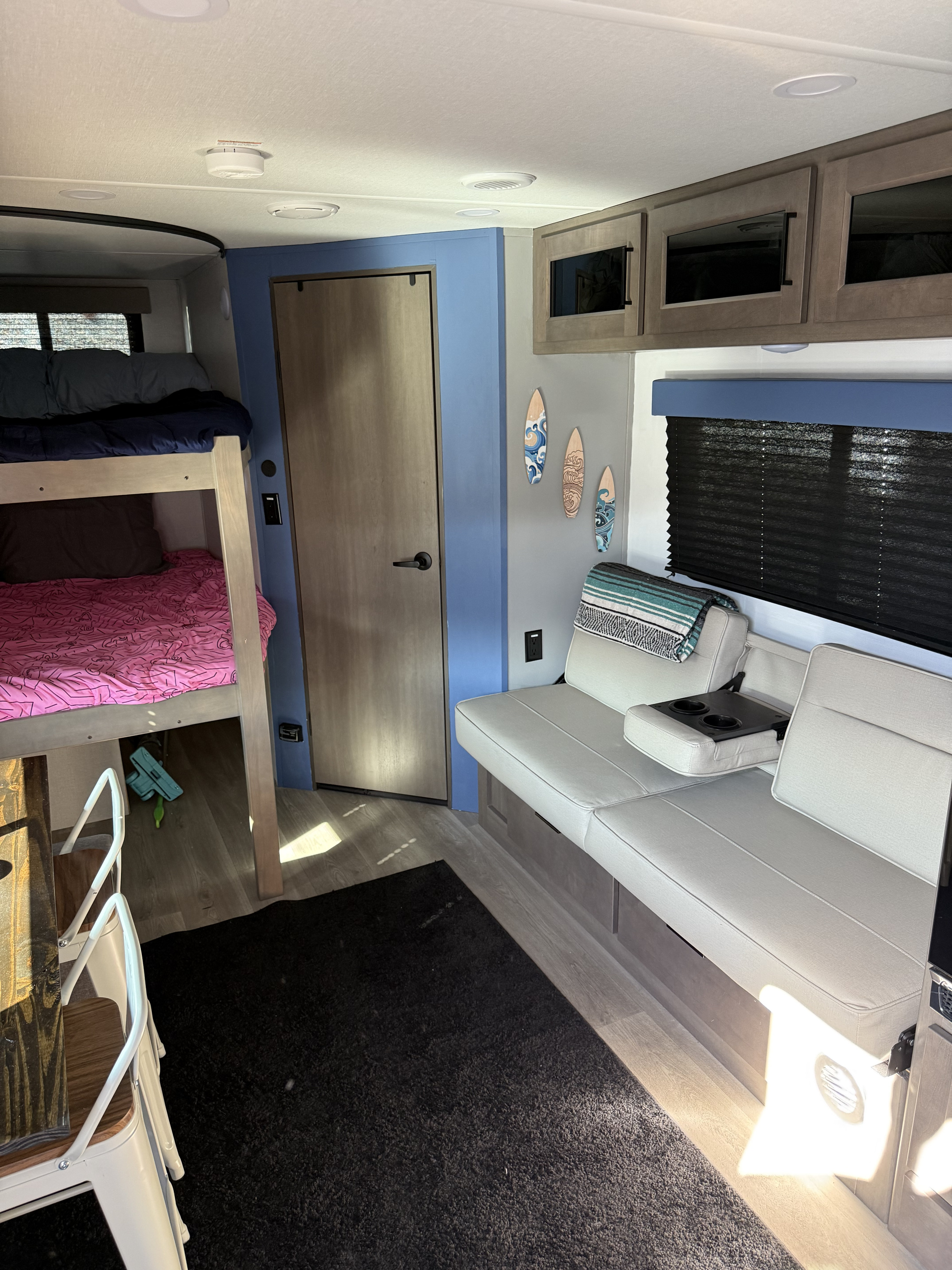 Inside an RV rental: a modern living area features bunk beds, a comfortable sofa, and overhead cabinets.. Grand Design Transcend Xplor 2024