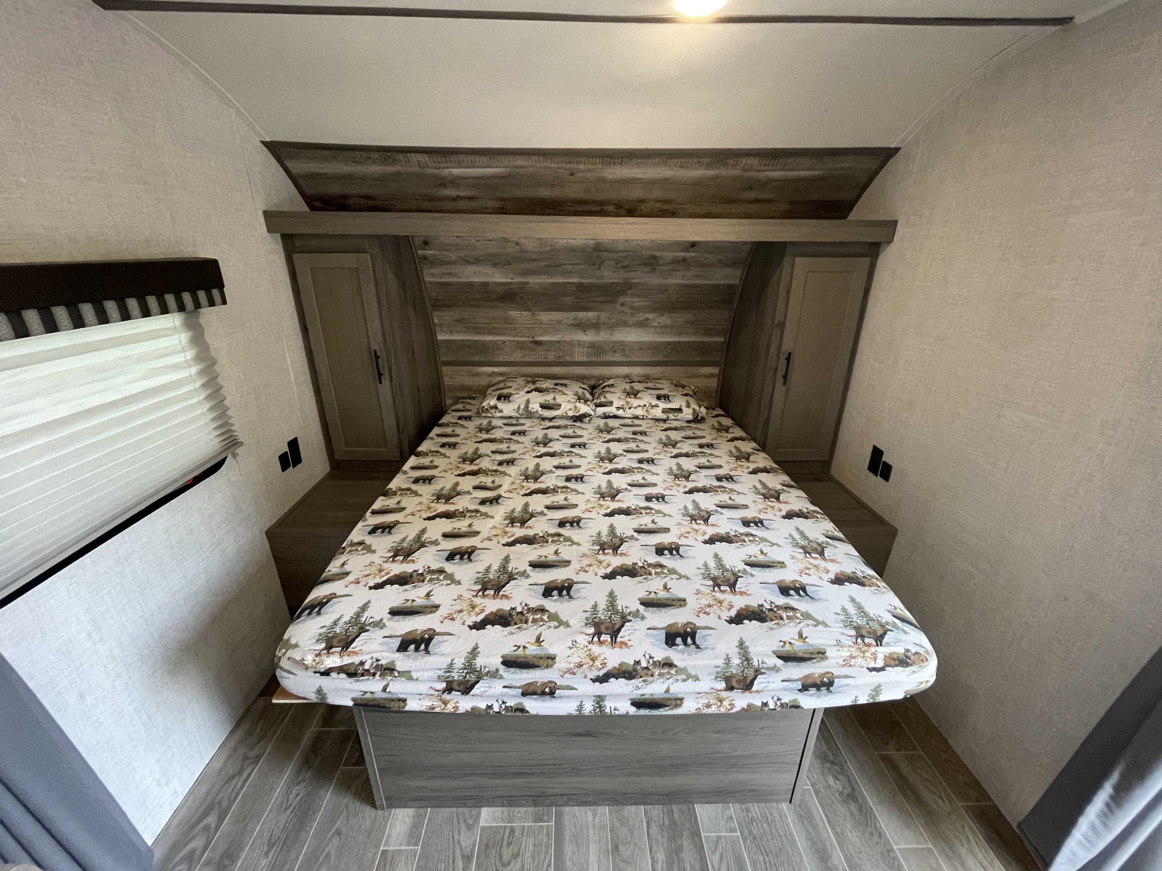 This cozy RV rental bedroom features nature-themed bedding, built-in cabinets, and a window, ideal for comfortable travel.. Gulf Stream Enlighten 2021