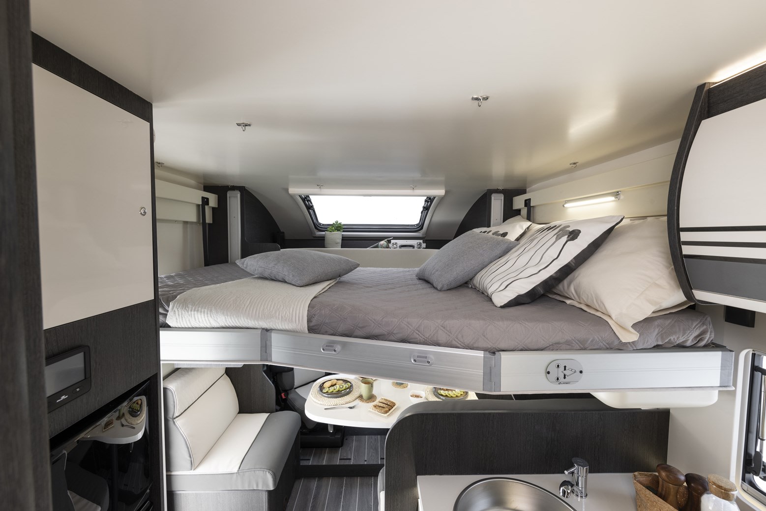 This RV rental interior highlights clever design: a drop-down bed suspended above a dining area and sink, optimizing compact living.. Roller Team Zefiro 685 2024